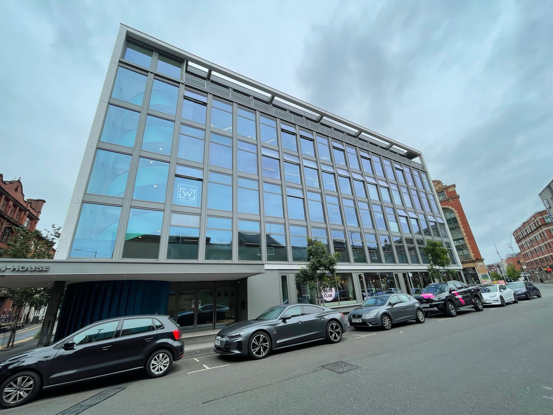 A row of cars are parked in front of a large building.