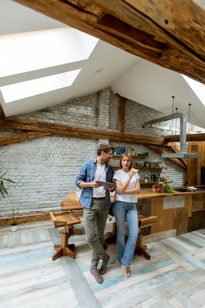 Two people standing in a rustic kitchen with exposed beams, reading a recipe together.
