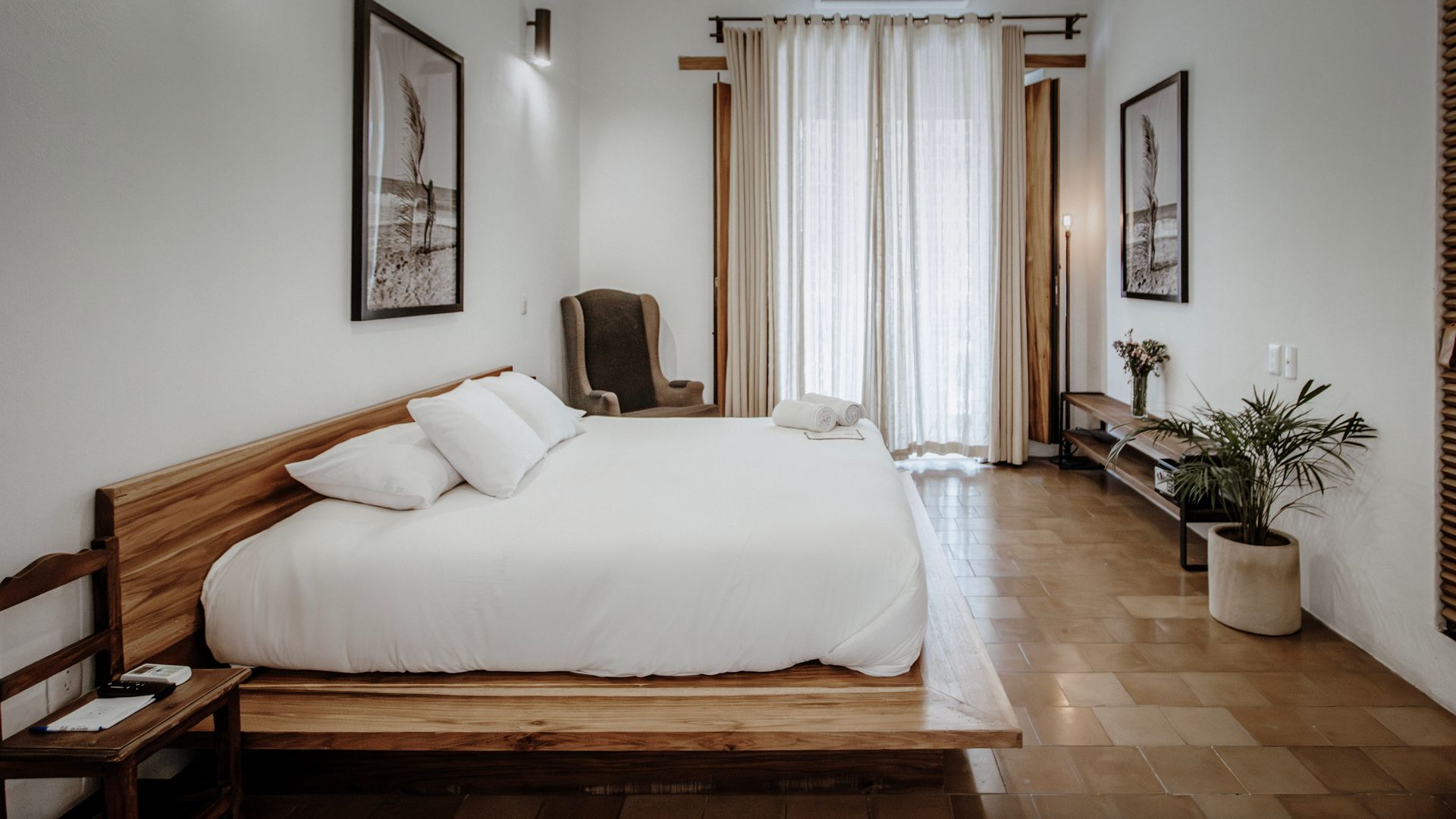 Minimalist bedroom with a wooden platform bed, white bedding, and sheer curtains by a bright window.