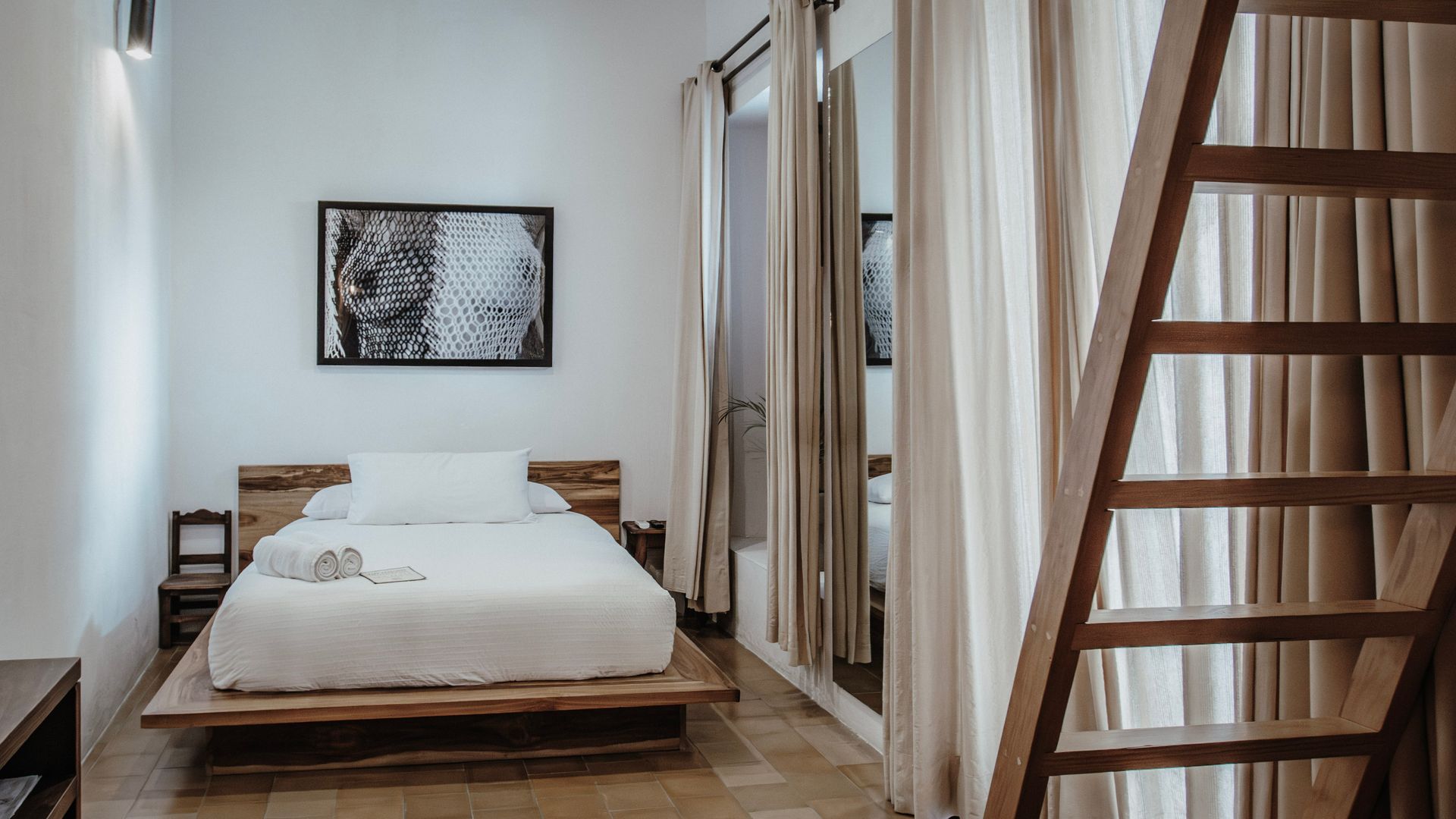 Minimalist bedroom with wooden bed, white bedding, curtains, and a ladder on the right