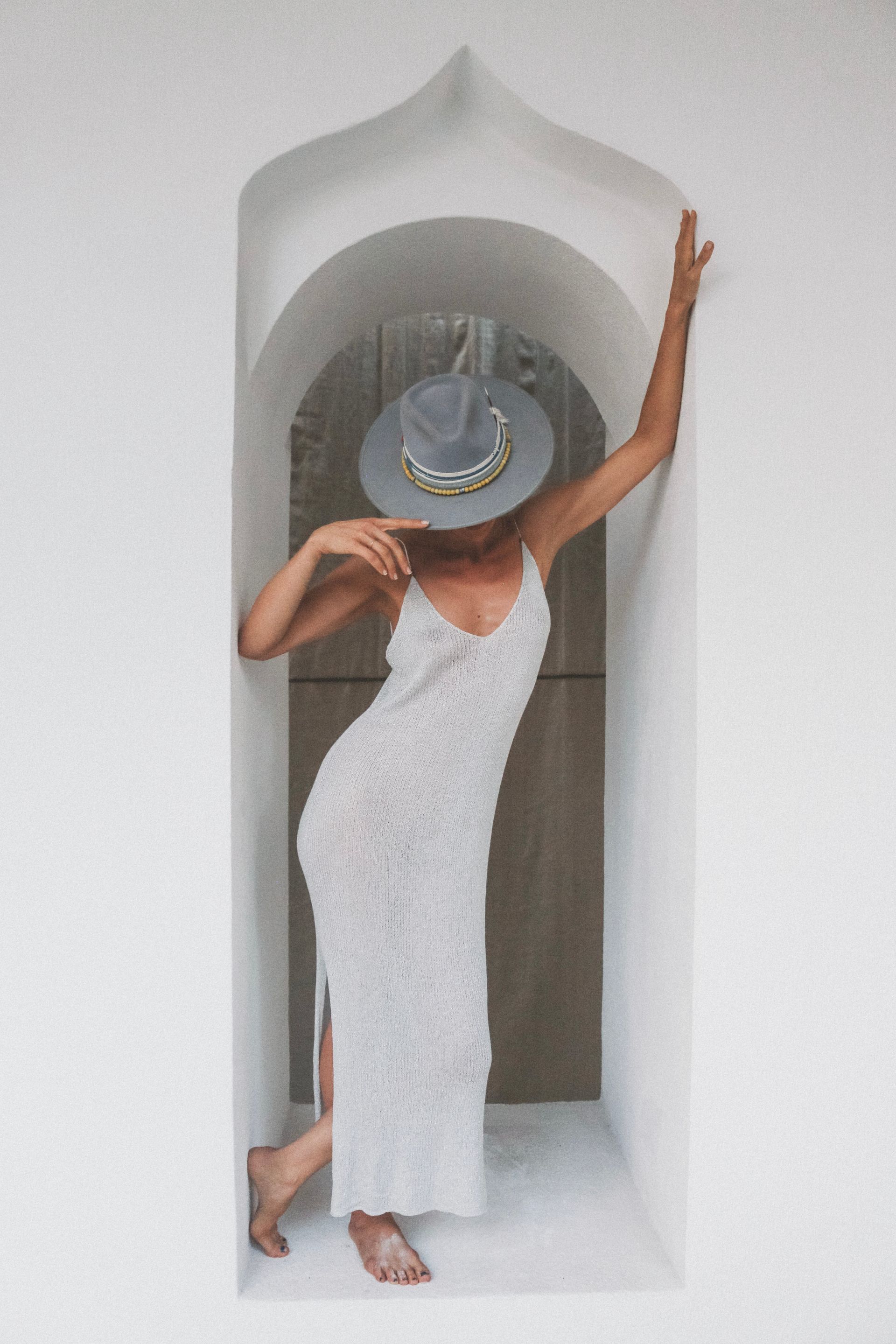 Woman in a white dress and wide-brimmed hat posing in a white arched doorway