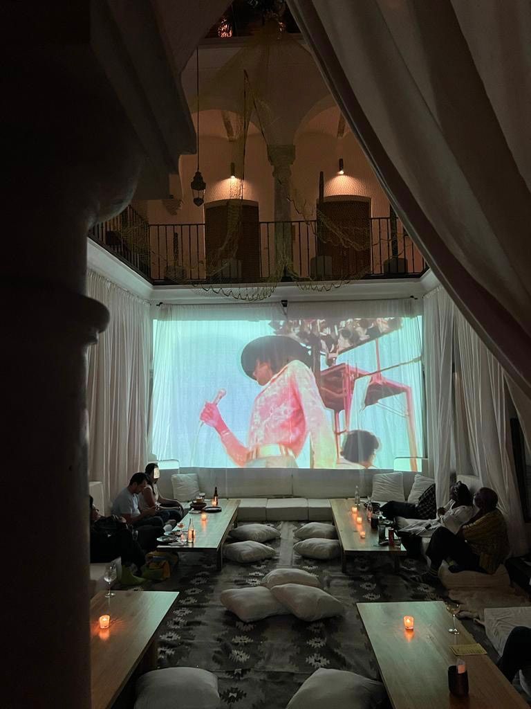 Dim lounge with draped curtains, candles, and a projection of a violin performance on a large screen.