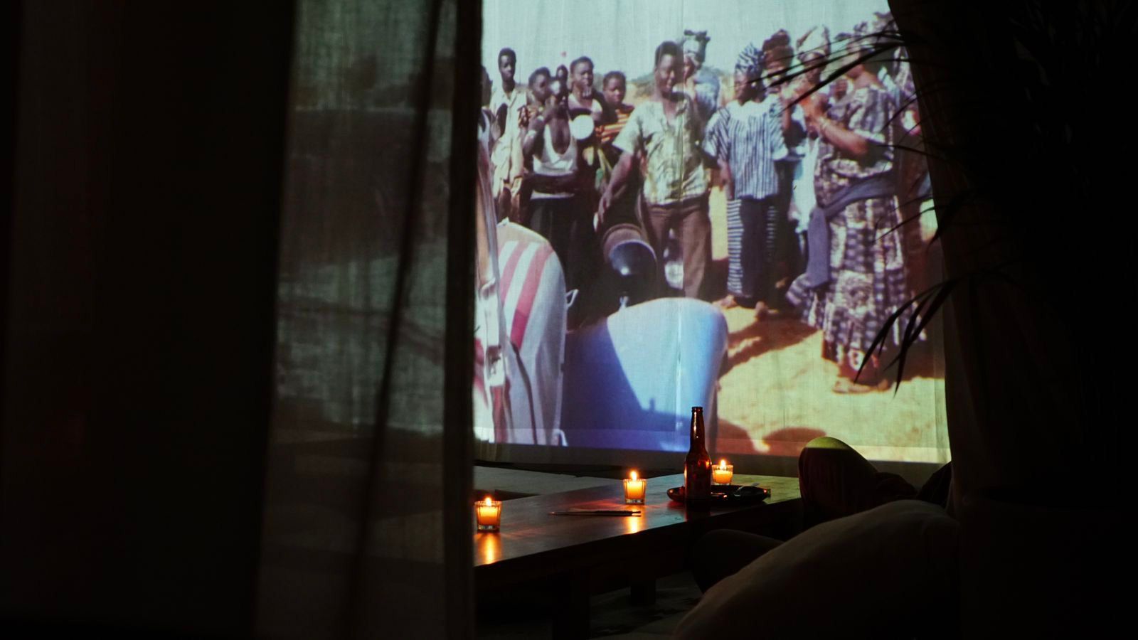 Projected group photo on a screen in a dim room, with curtains and candlelight in the foreground
