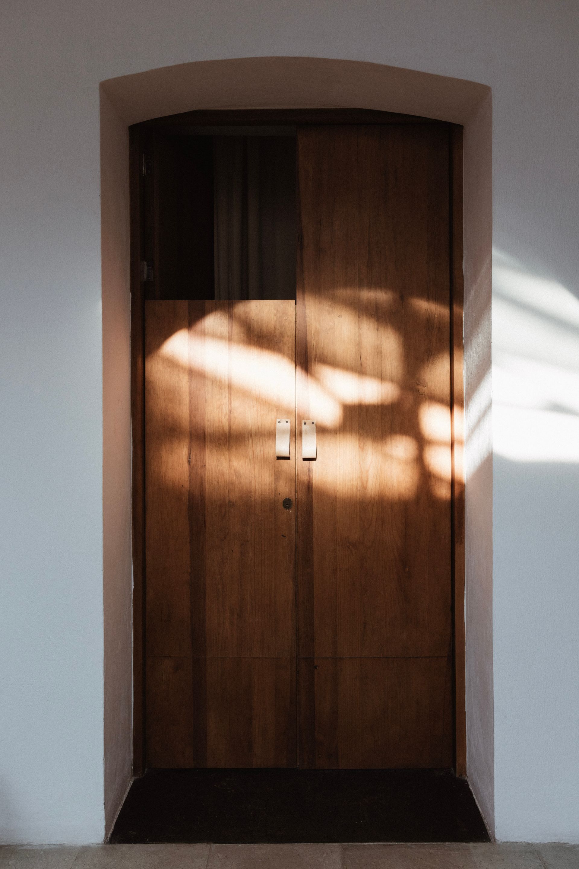 Wooden double door in a white stucco wall, lit by sunlight and shadow.