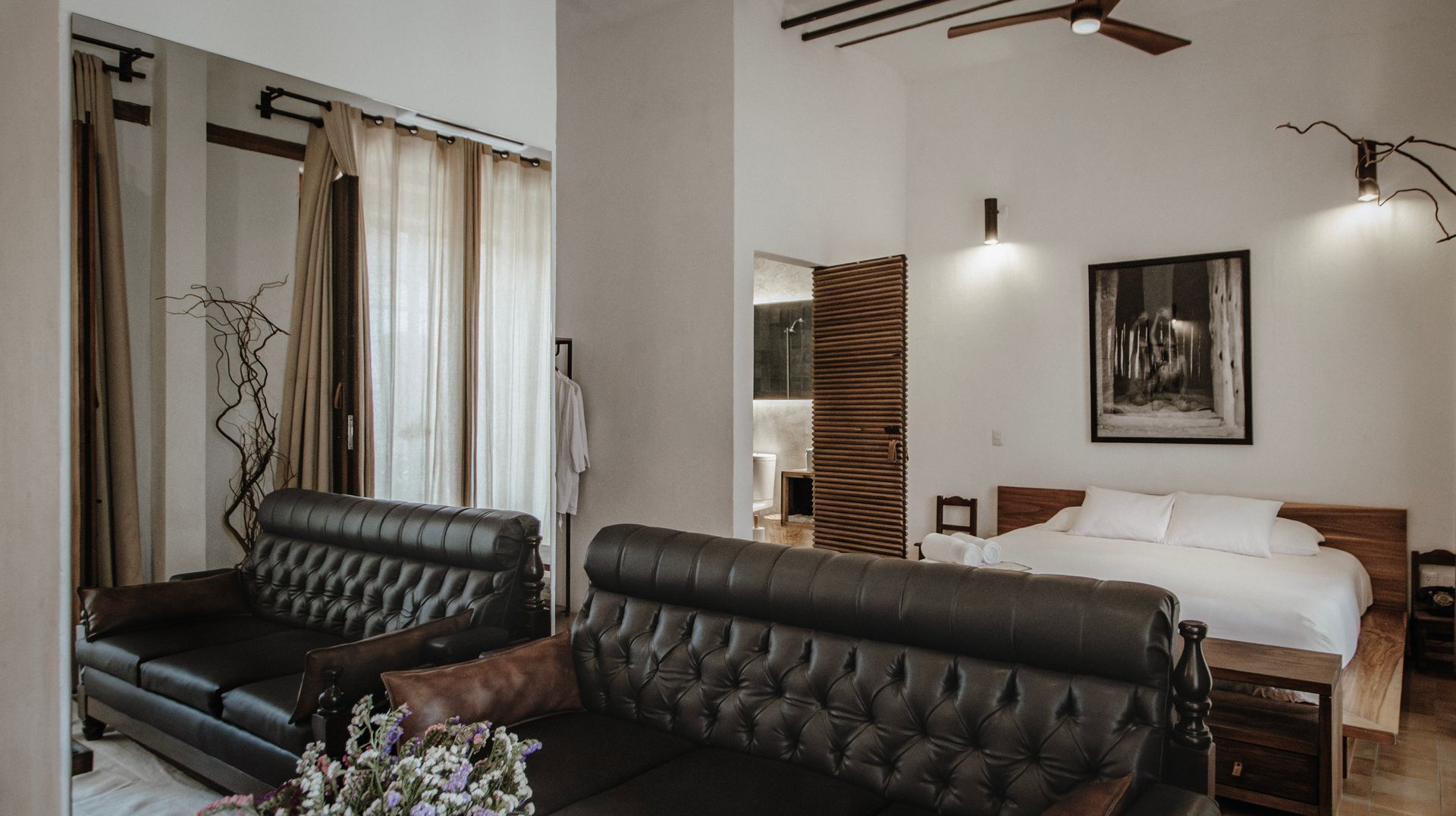 Modern bedroom with black tufted sofa, white bed, wall art, and mirrored closet doors