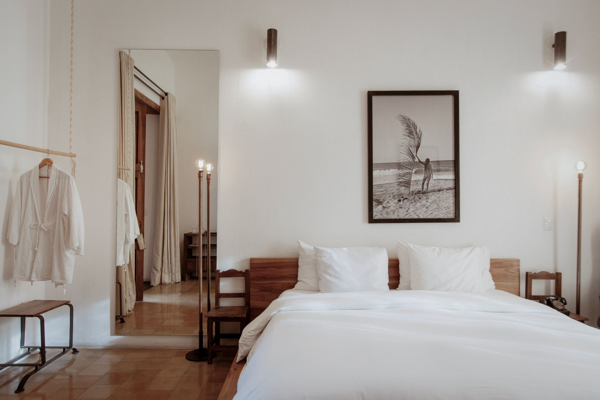 Minimalist bedroom with white bed, wooden furniture, wall art, and warm sconces