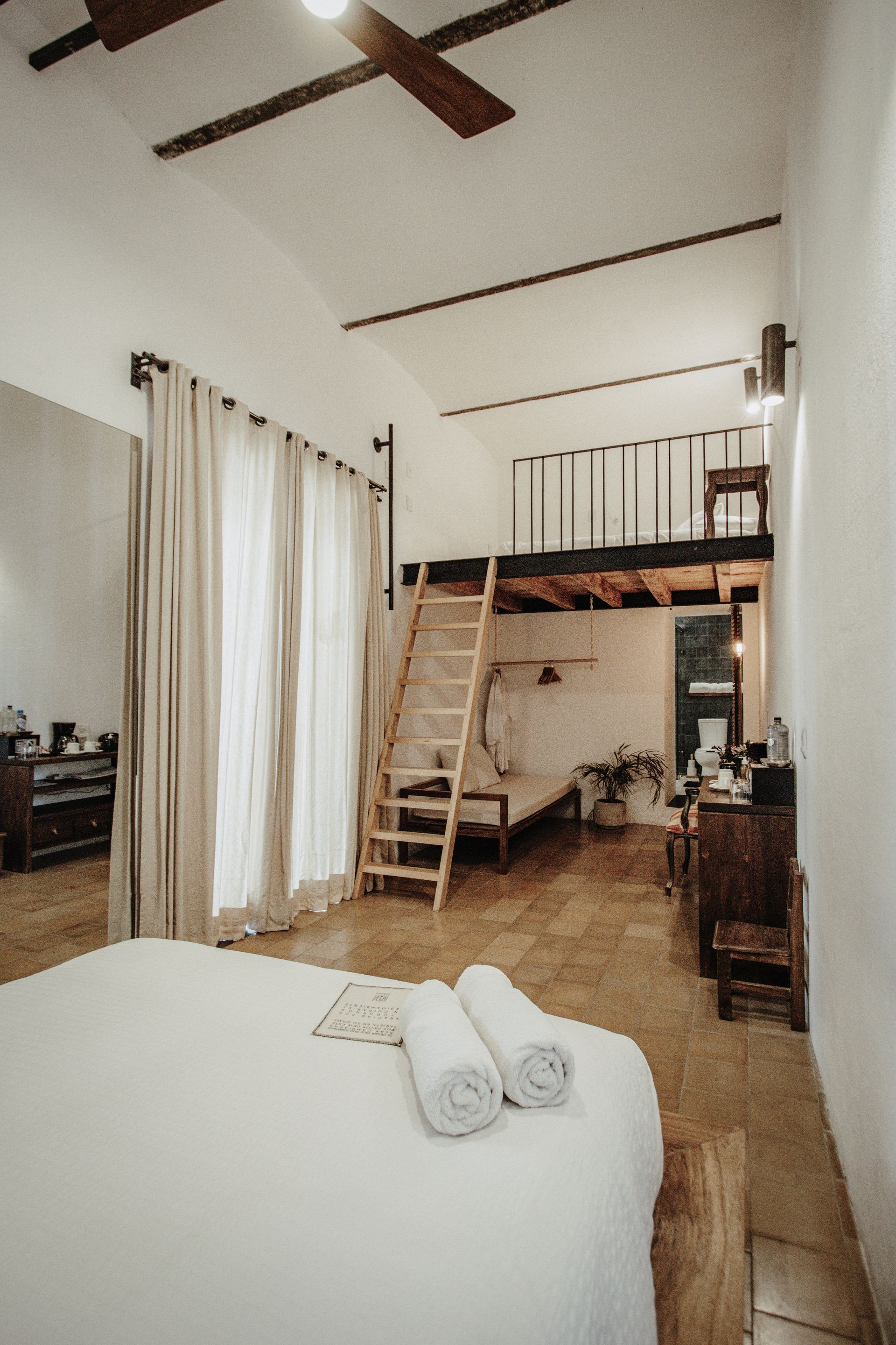 Loft bedroom with white bedding, wood floors, curtains, ladder, and mezzanine railing