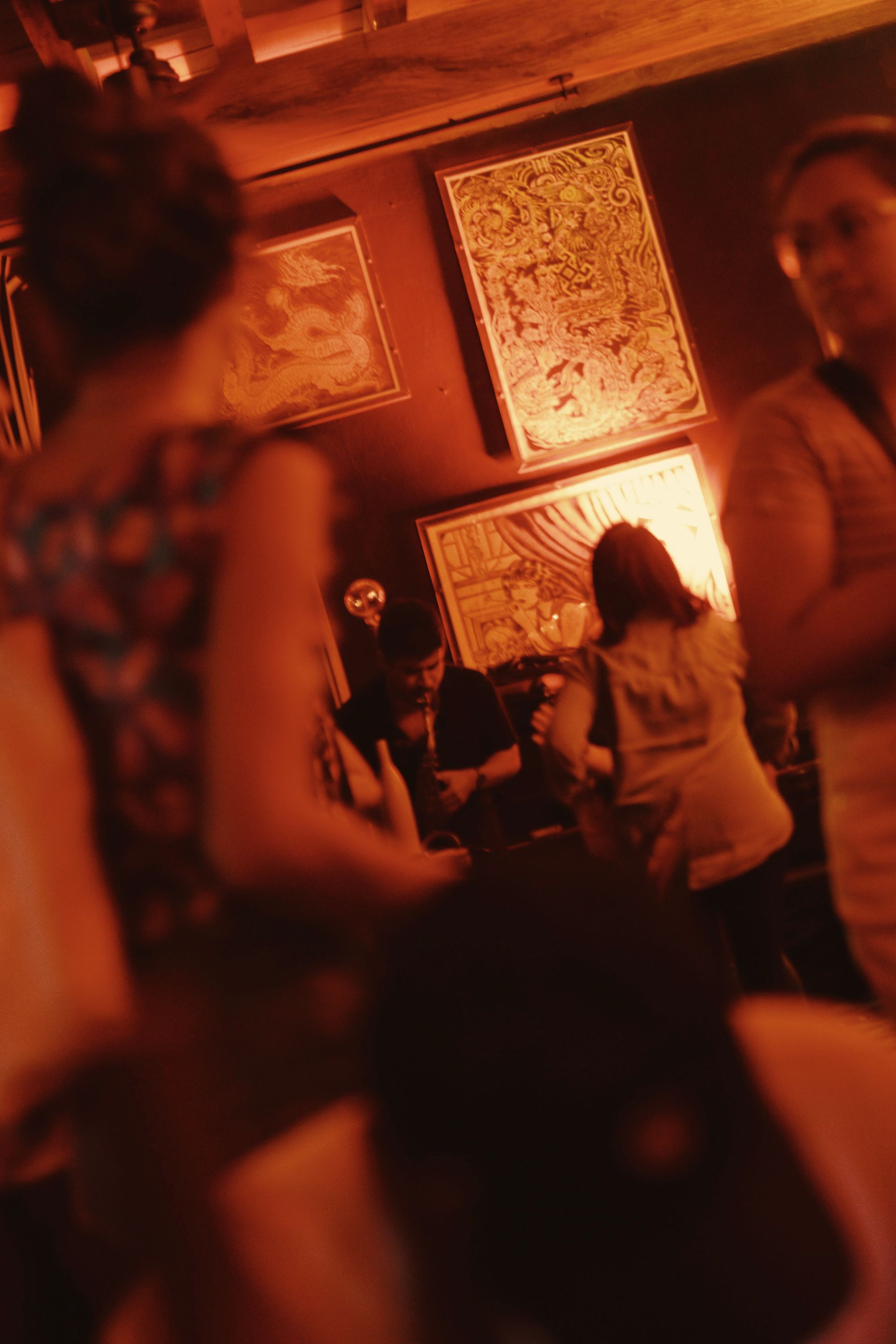 People mingling in a dim, warm-lit room with framed artwork on the wall.