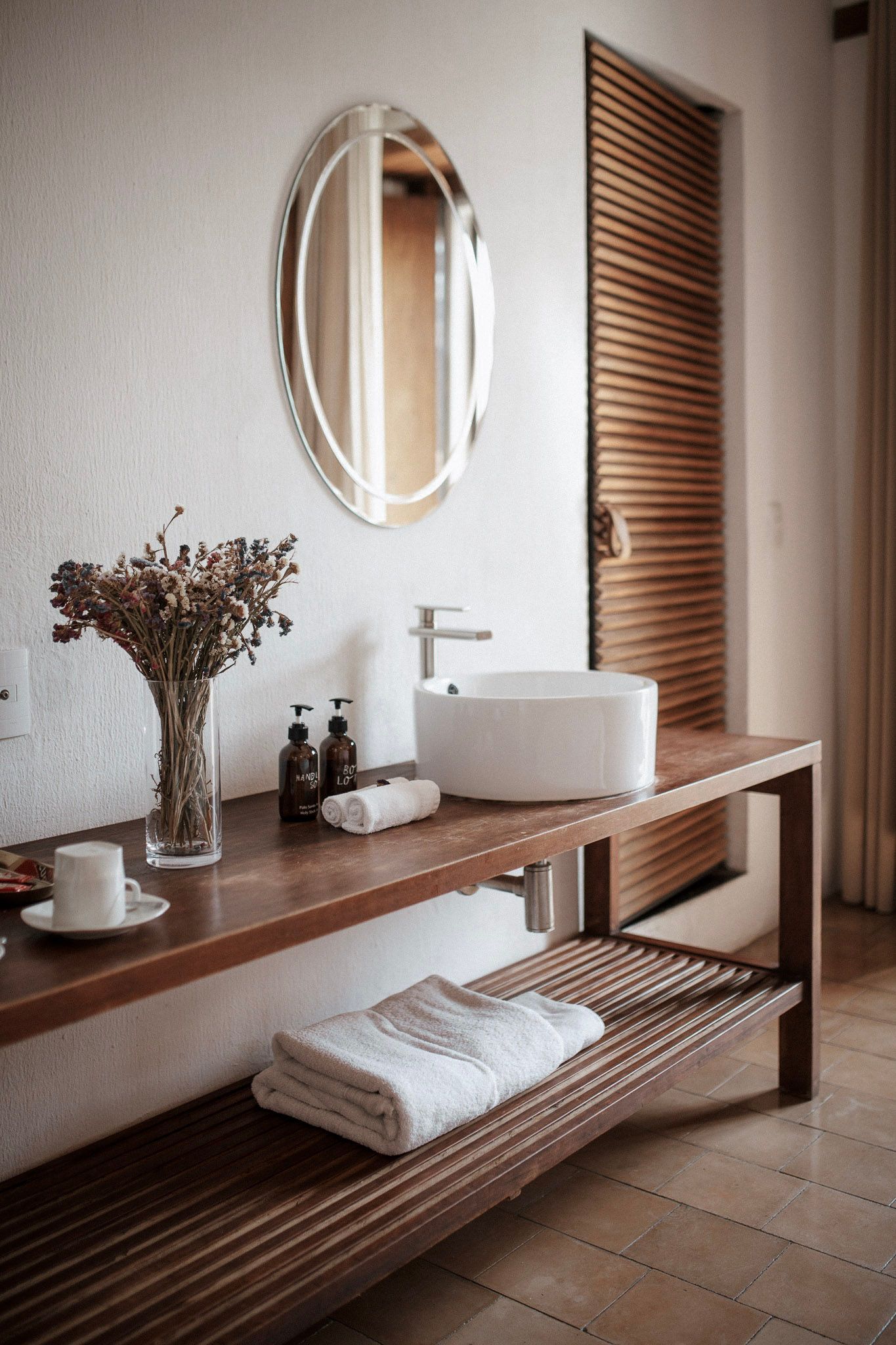 Modern bathroom vanity with oval mirror, white sink, wood counter, woven shelf, and soft neutral tones