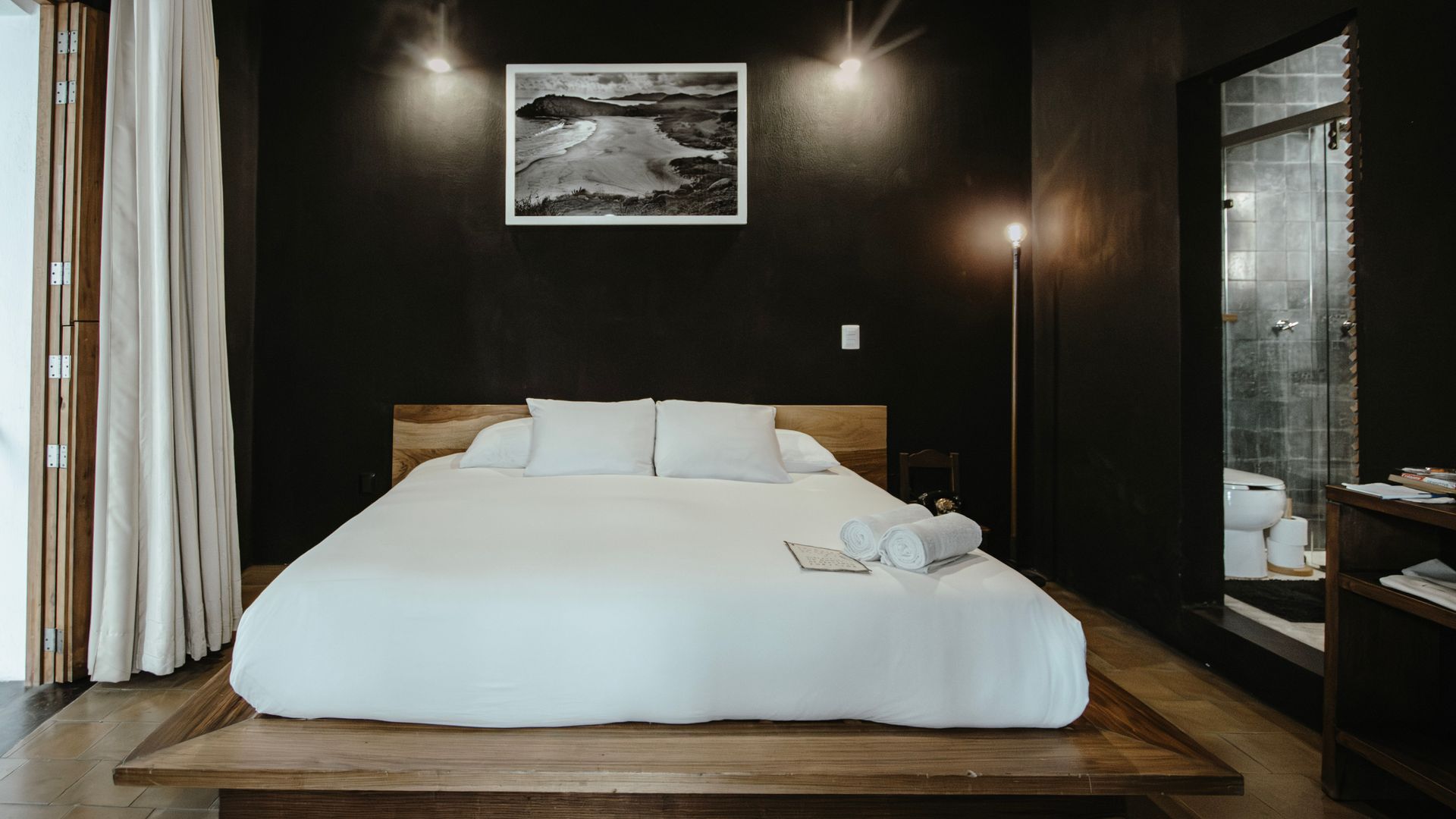 Modern bedroom with a low white bed, dark walls, wood floor, and soft wall sconces