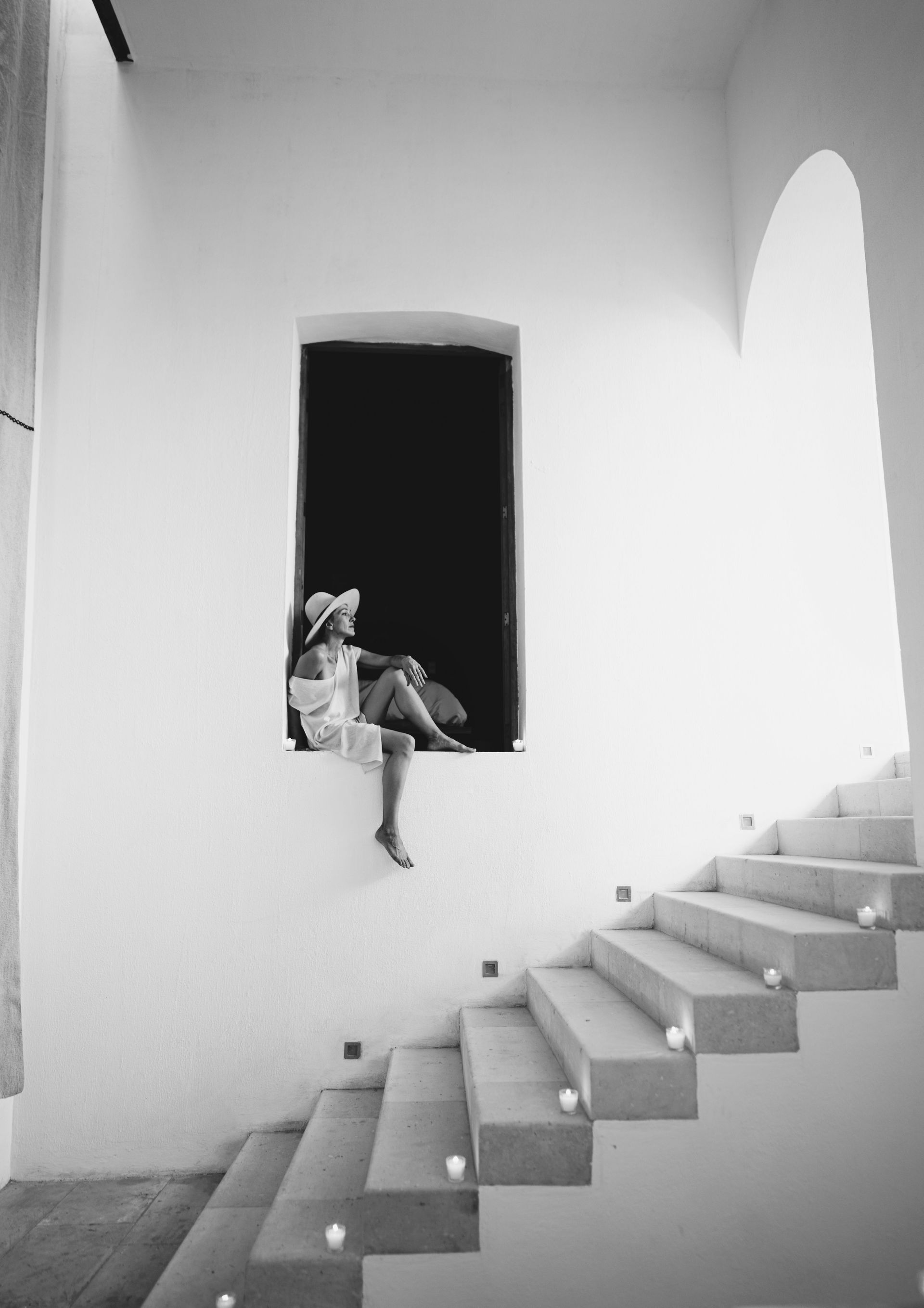 Person sitting in a dark window opening above a staircase in a bright white room