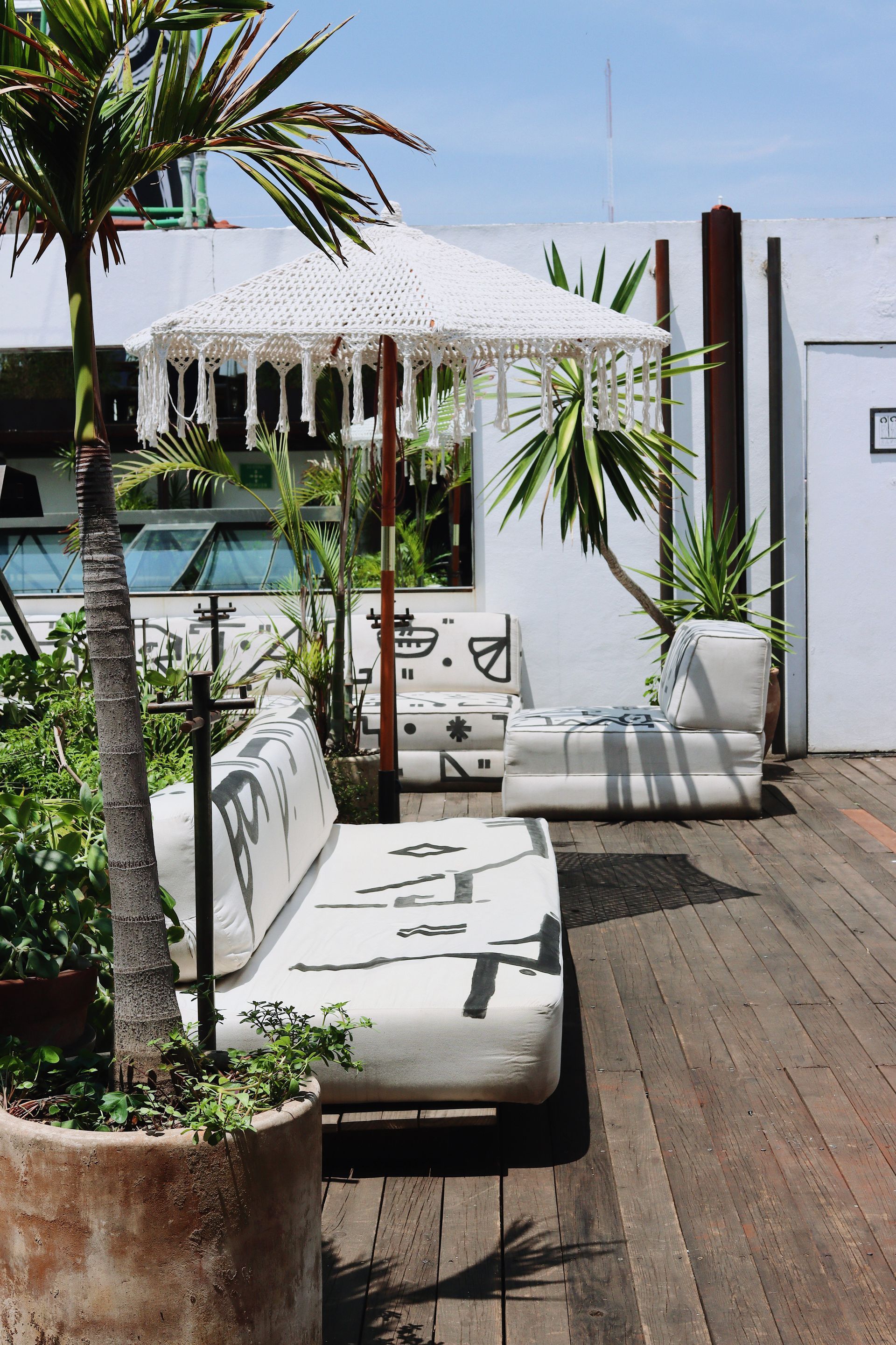 Patio lounge with white daybeds, potted palms, and wooden decking beside a pool and white pergola.