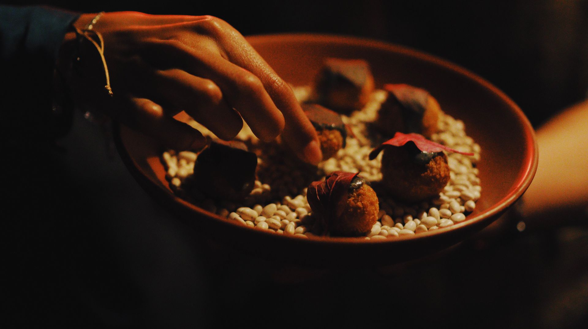 Hand reaching into a bowl of rice and curry in warm, dim light