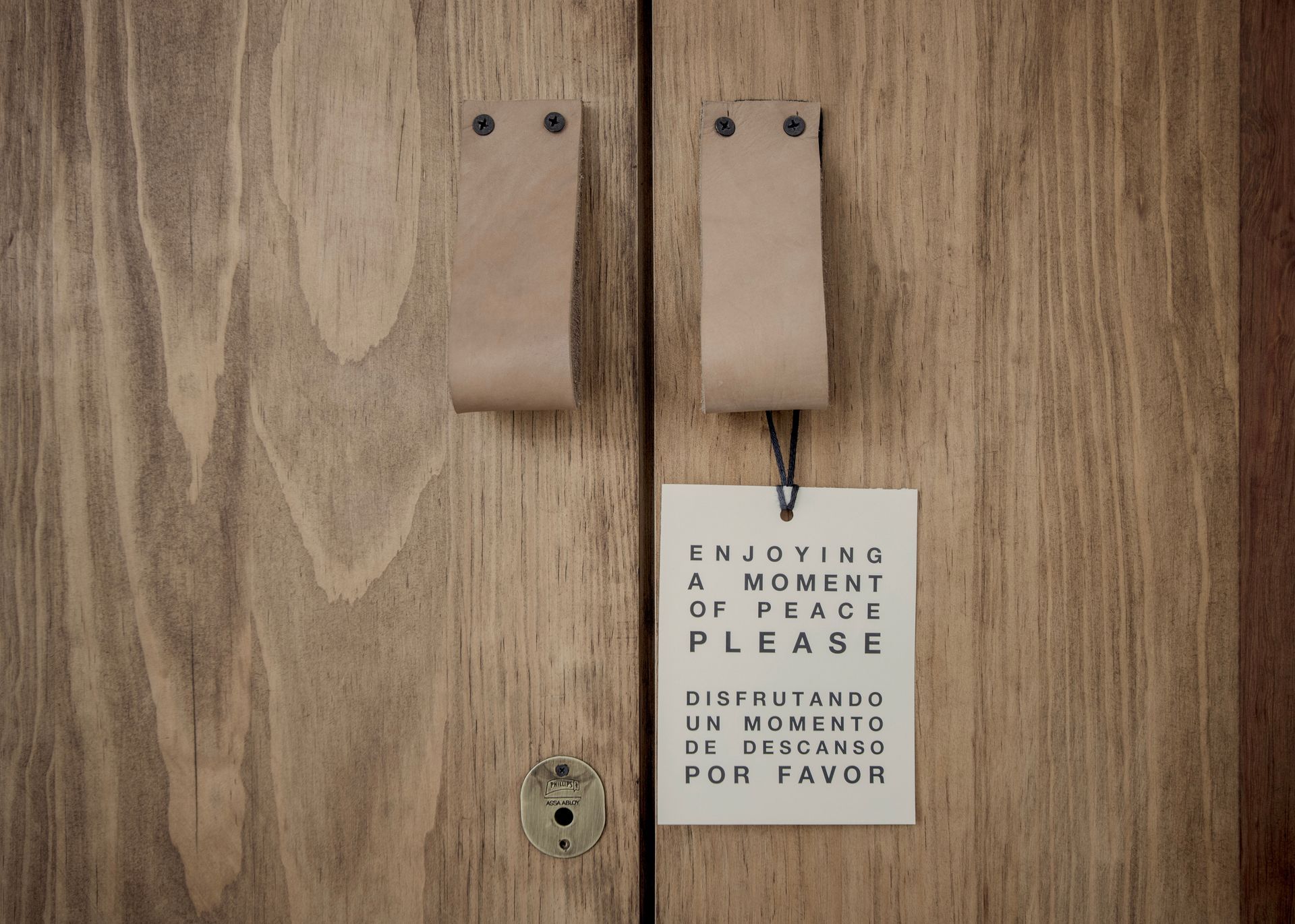 Two tan door handles on a wooden door with a sign warning not to open unless instructed.
