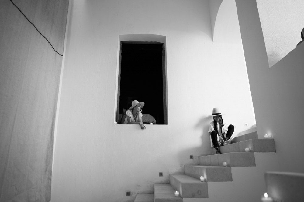 Two people on a white stairwell, one sitting in a window opening and one on the steps with a guitar.