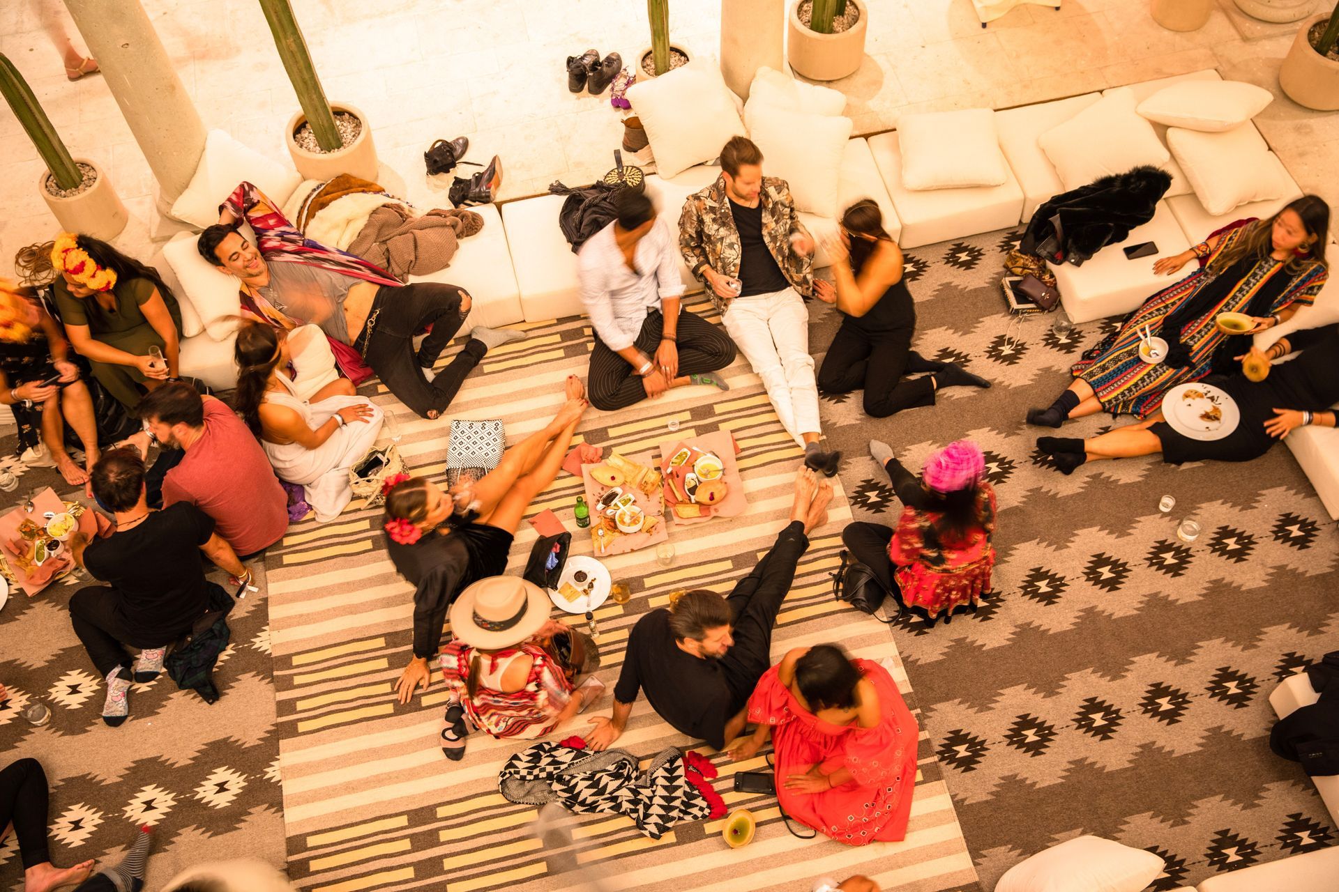 People seated on floor cushions around a patterned rug in a bright indoor gathering space.