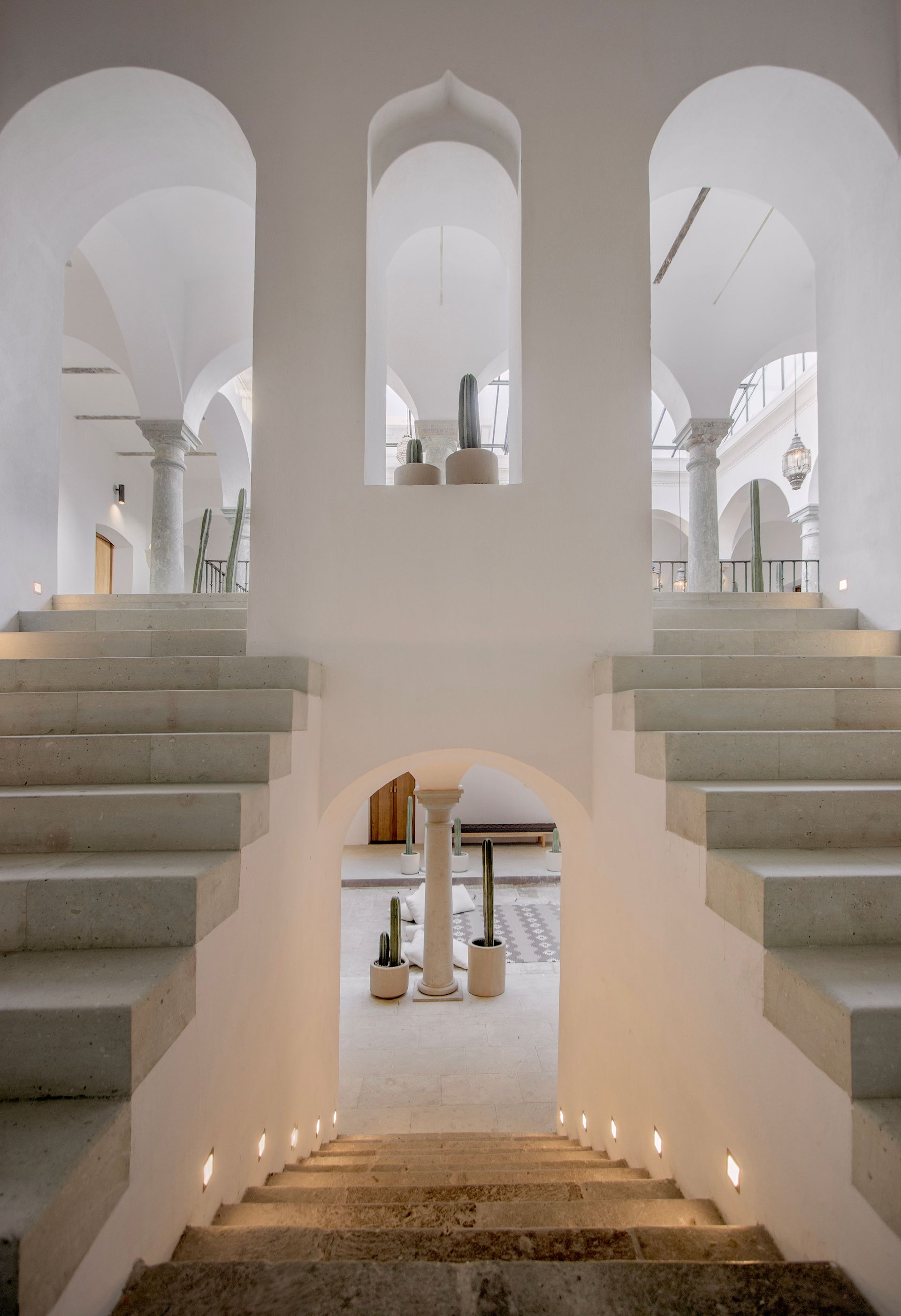 White stairwell with symmetrical arches, stone steps, and warm lights in a minimalist interior