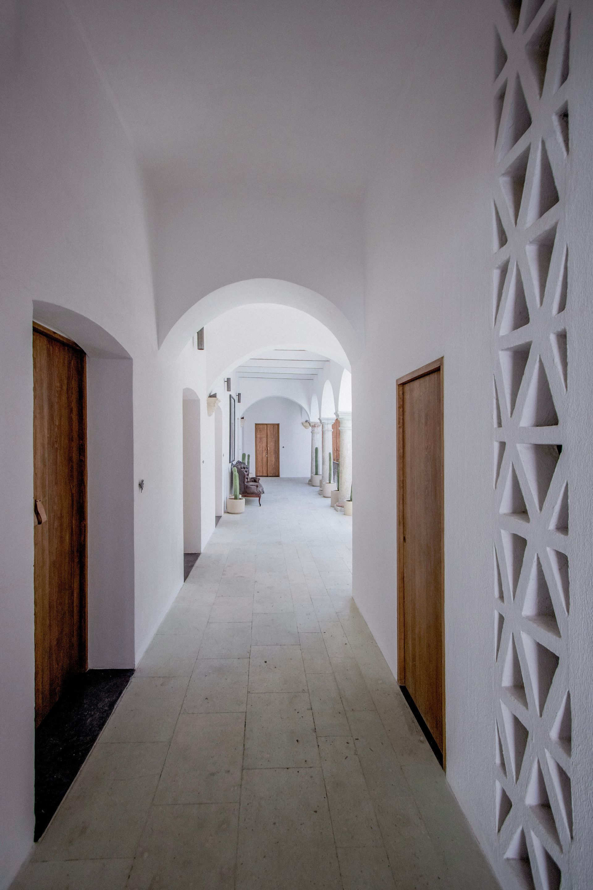 White arched hallway with doors on both sides and a patterned wall on the right