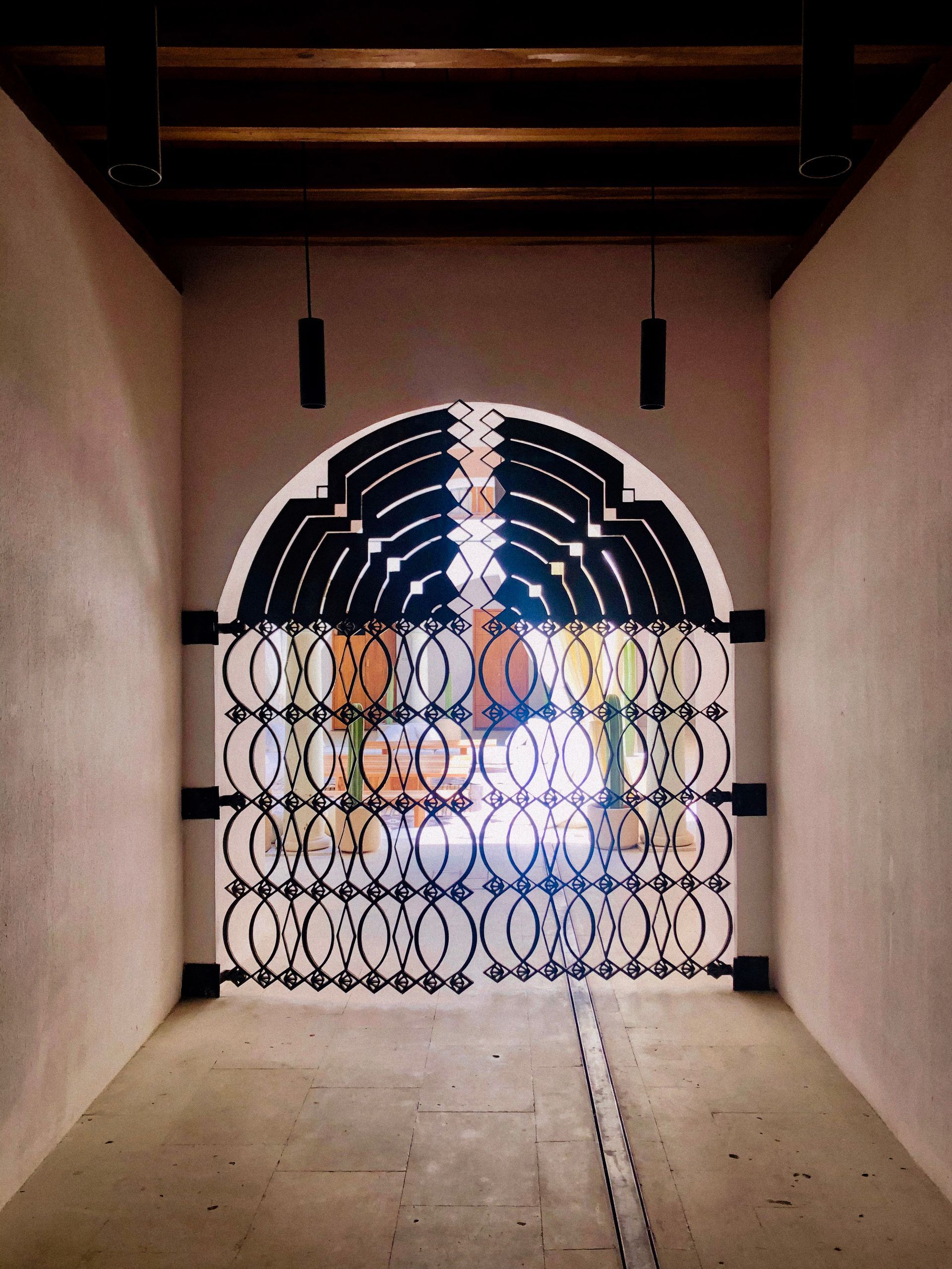 Indoor corridor with an ornate black metal gate and bright light at the far end