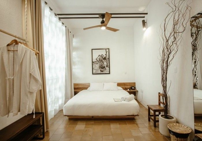 Bright minimalist bedroom with a white bed, wooden accents, hanging clothes, and a ceiling fan