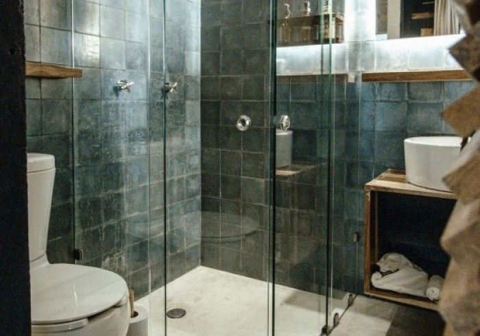 Modern bathroom with glass shower, dark tile walls, toilet, and wooden shelf with towels