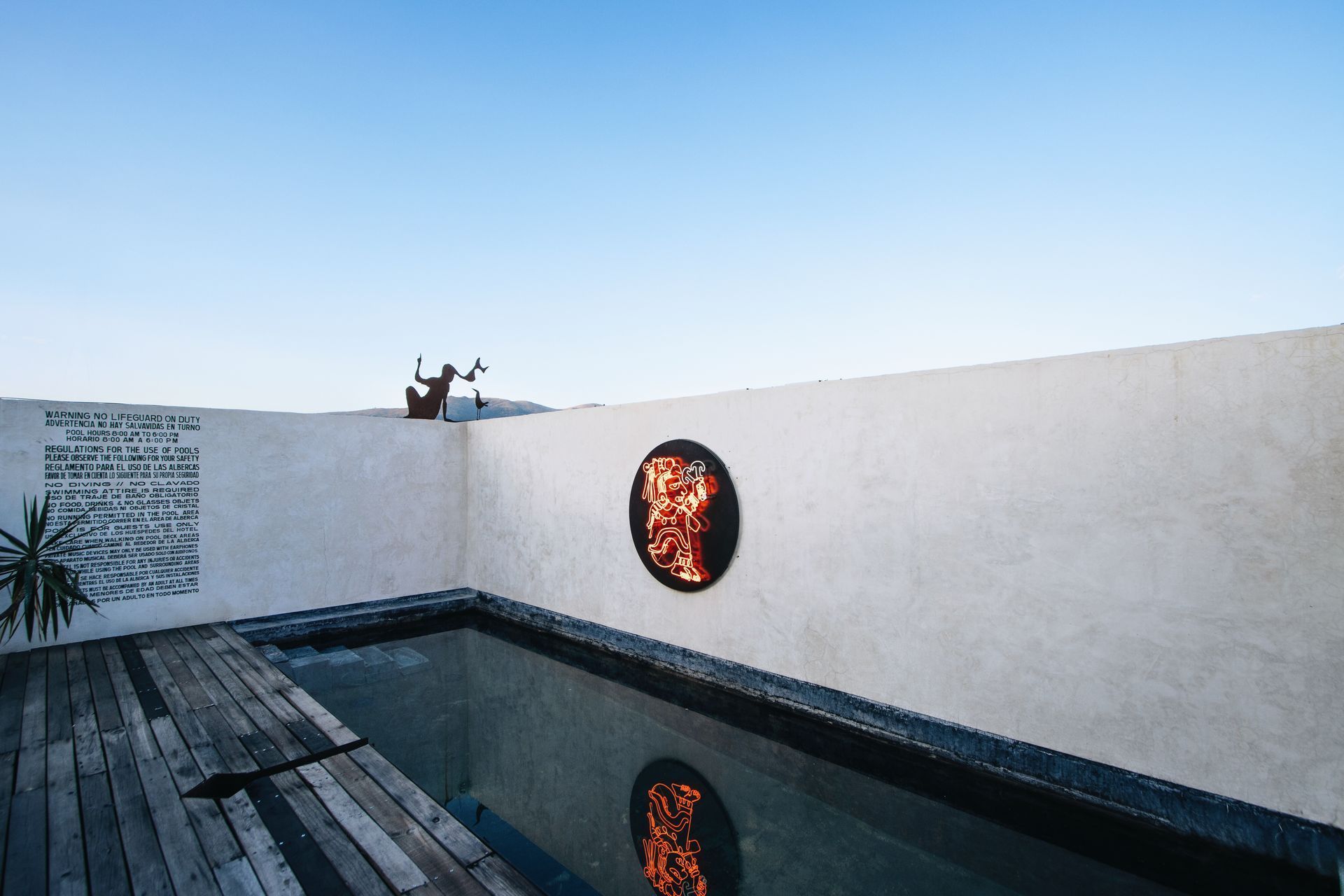 Modern white courtyard with a narrow pool reflecting a circular wall art piece under a blue sky