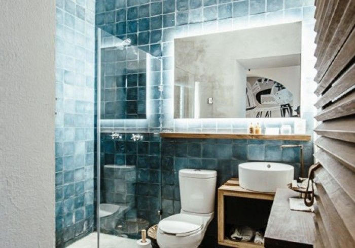 Modern bathroom with blue tile, toilet, sink, mirror, and wood slat wall