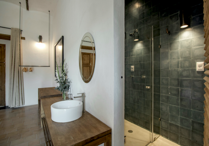 Modern bathroom with wooden vanity, oval mirror, white sink, and glass shower with dark tile walls