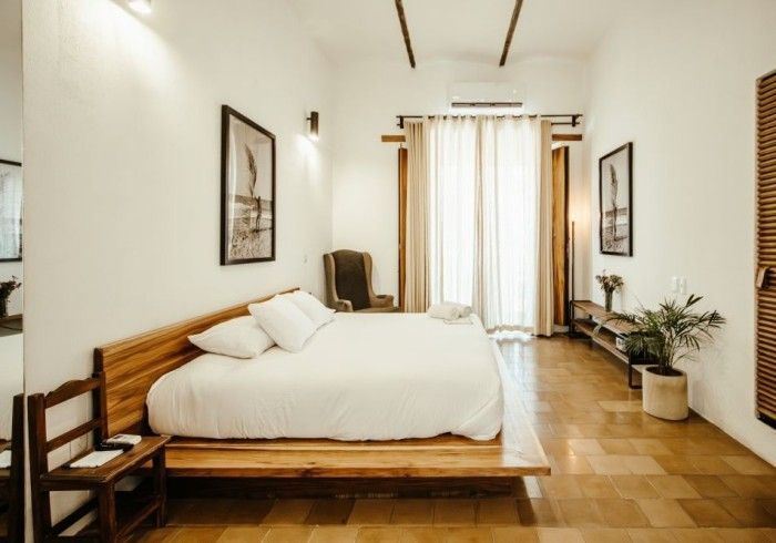 Bright minimalist bedroom with a wooden bed, white bedding, and curtains at the far window