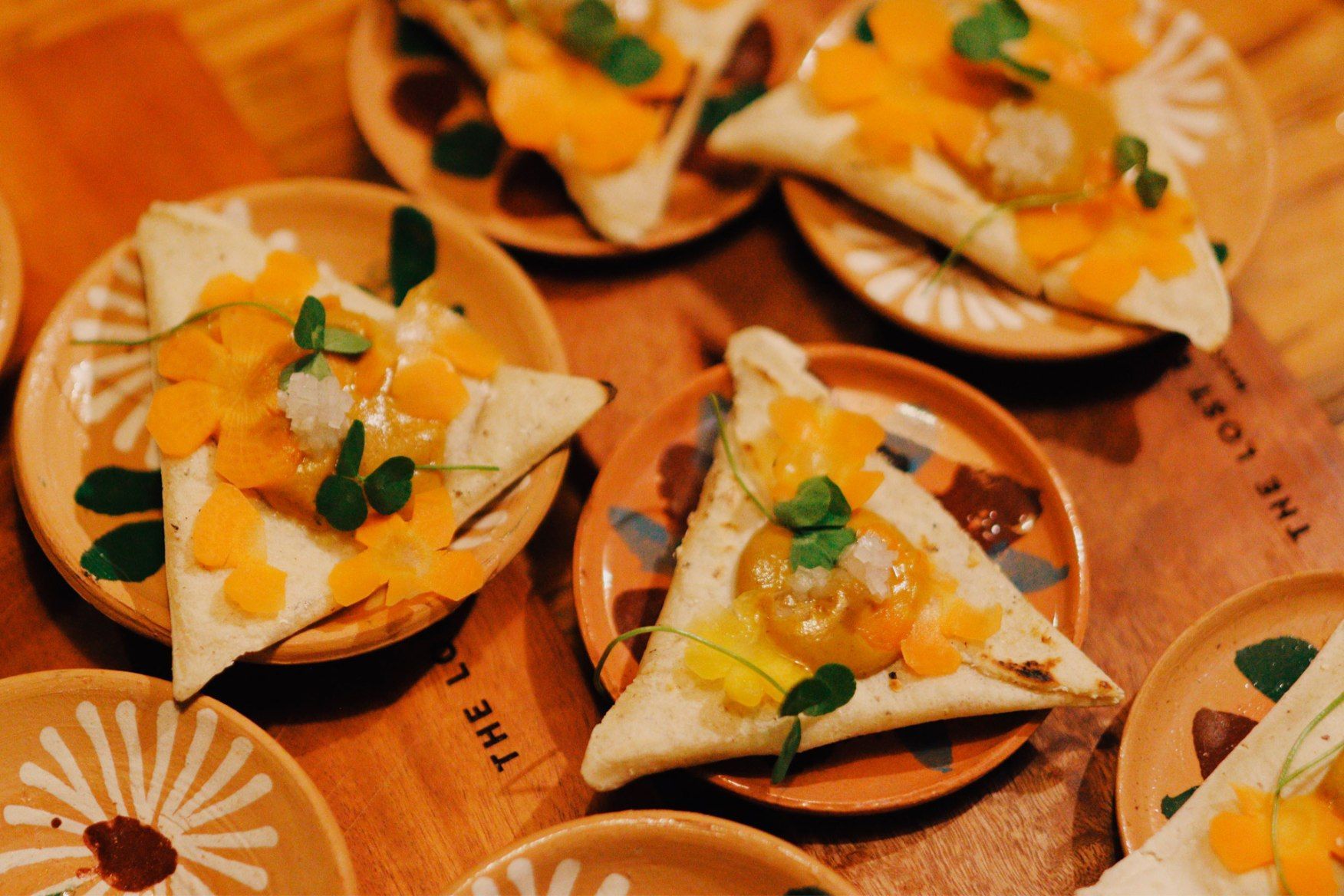 Triangular appetizers topped with orange garnish and green herbs on wooden plates