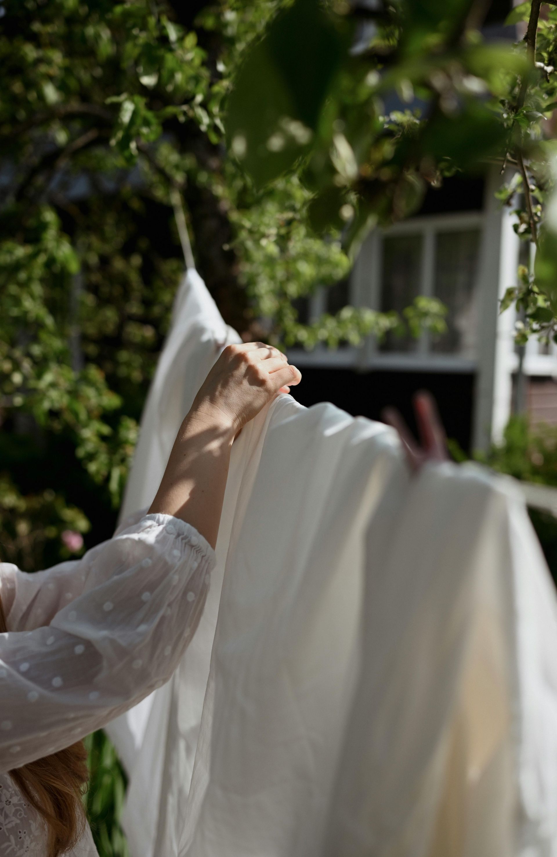 A woman is hanging white sheets on a clothes line.
