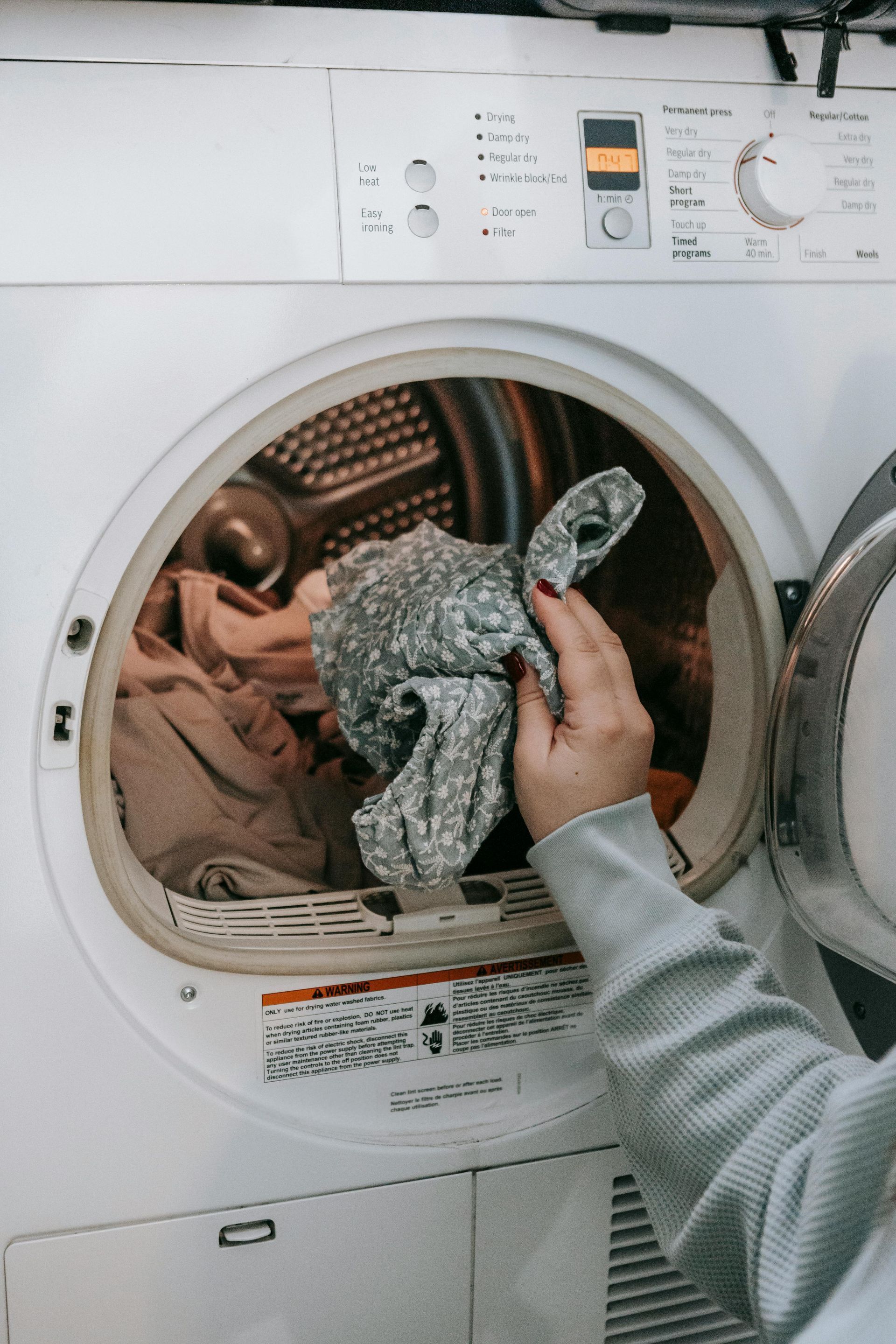 A person is putting clothes in a dryer.