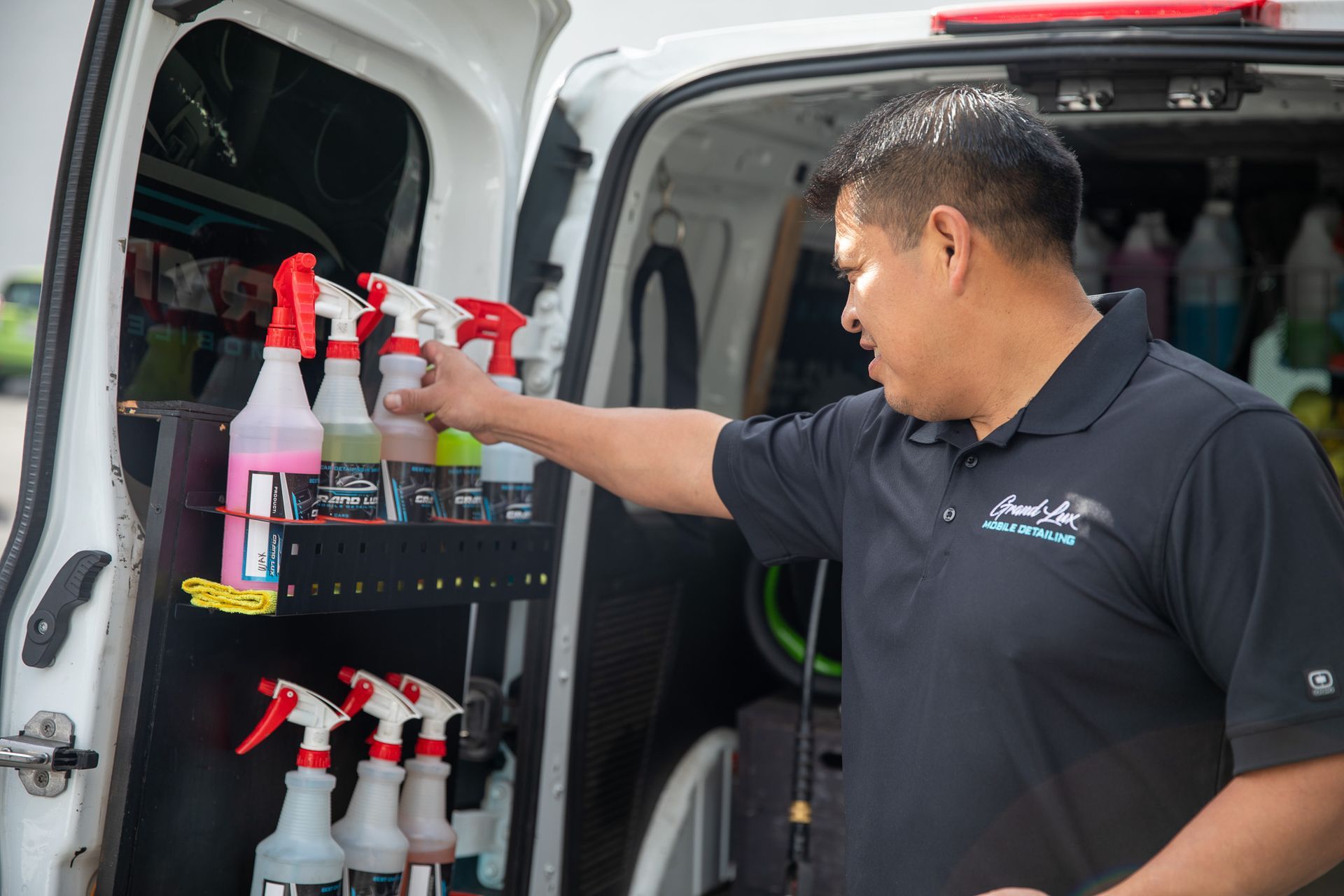 A man is standing in the back of a van holding a spray bottle.