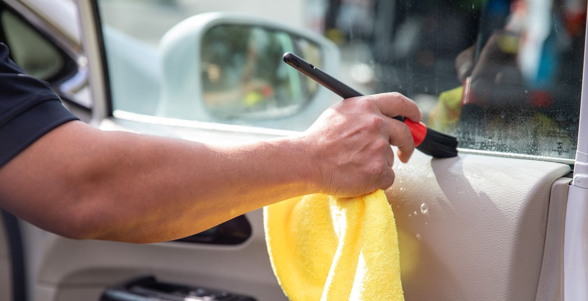 A man is cleaning the inside of a car with a towel and brush.