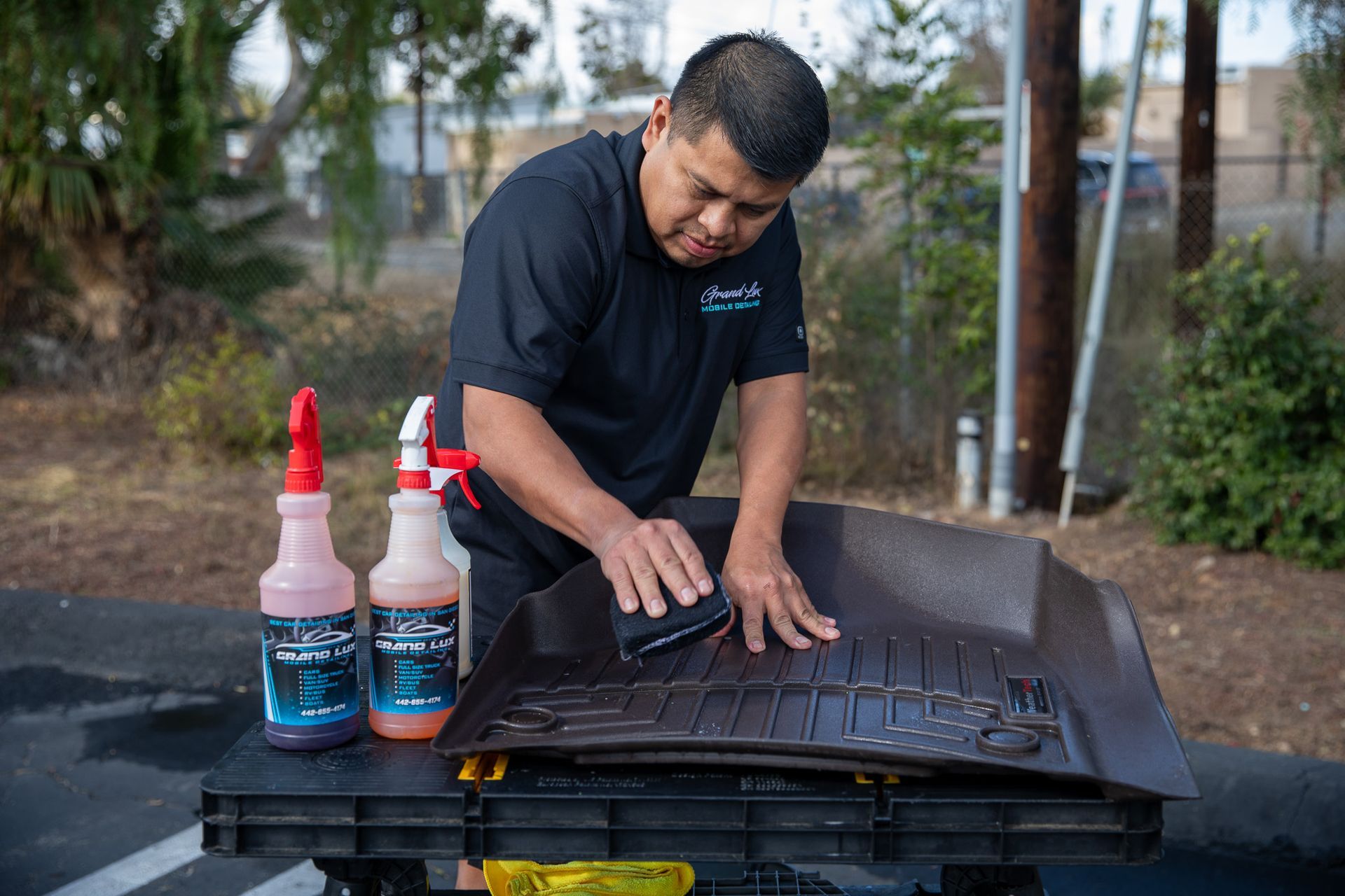 A man is cleaning a trunk mat on a table with spray bottles.