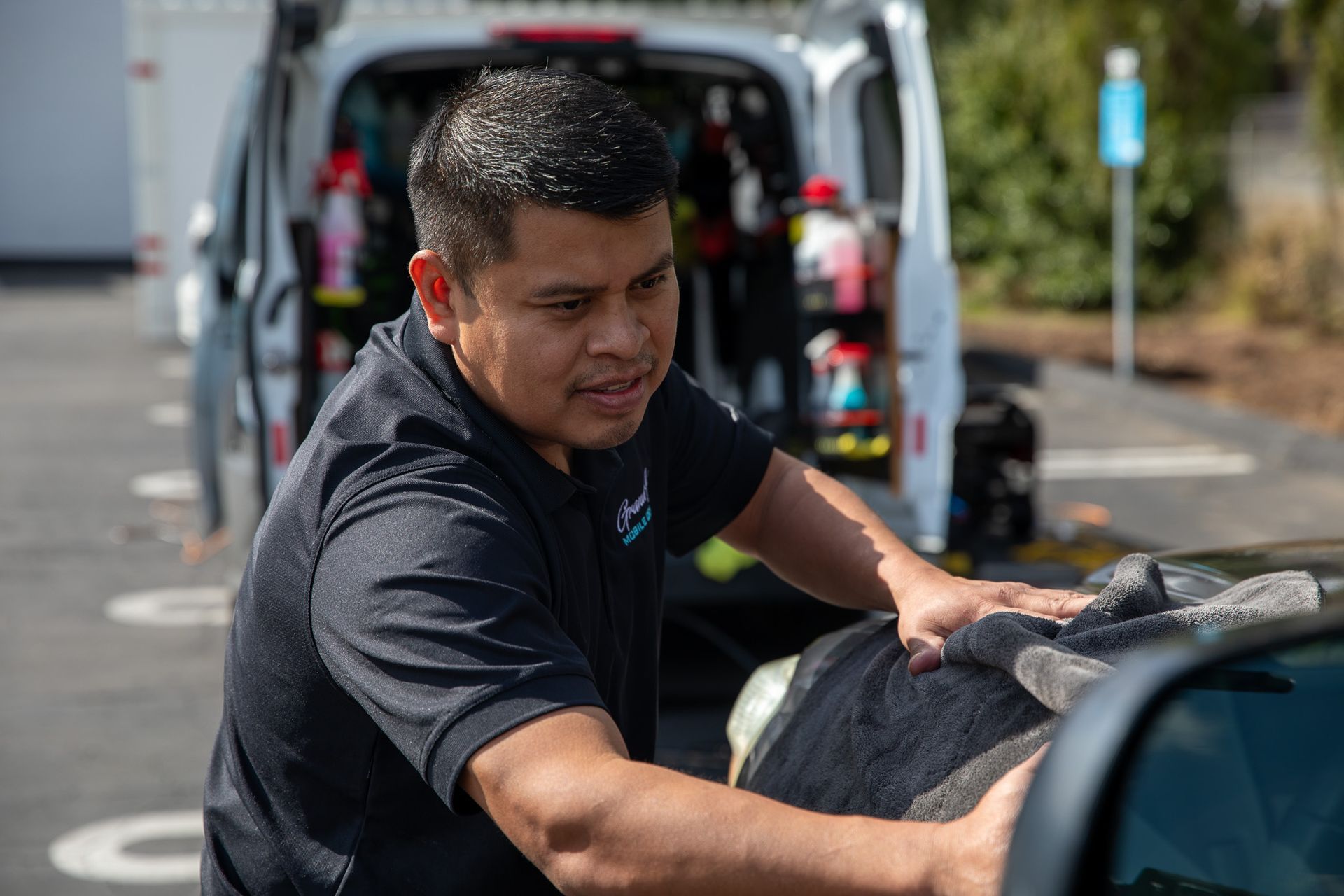 A man is cleaning a car with a towel in front of a van.