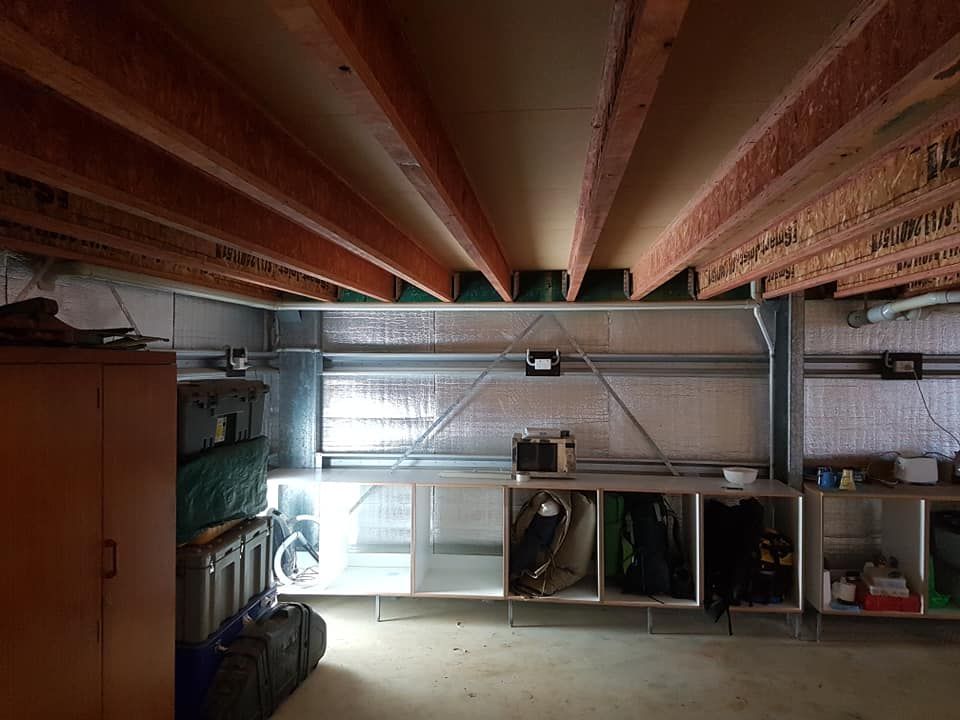 Interior of a garage or workshop with storage cabinets, shelving, and exposed ceiling beams. Silver insulation covers the walls.— Ionspark Electrical in Atherton, QLD