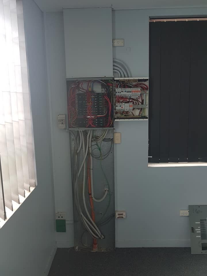 Electrical Panel With Exposed Wiring on a Blue Wall, Near a Window — Ionspark Electrical in Atherton, QLD