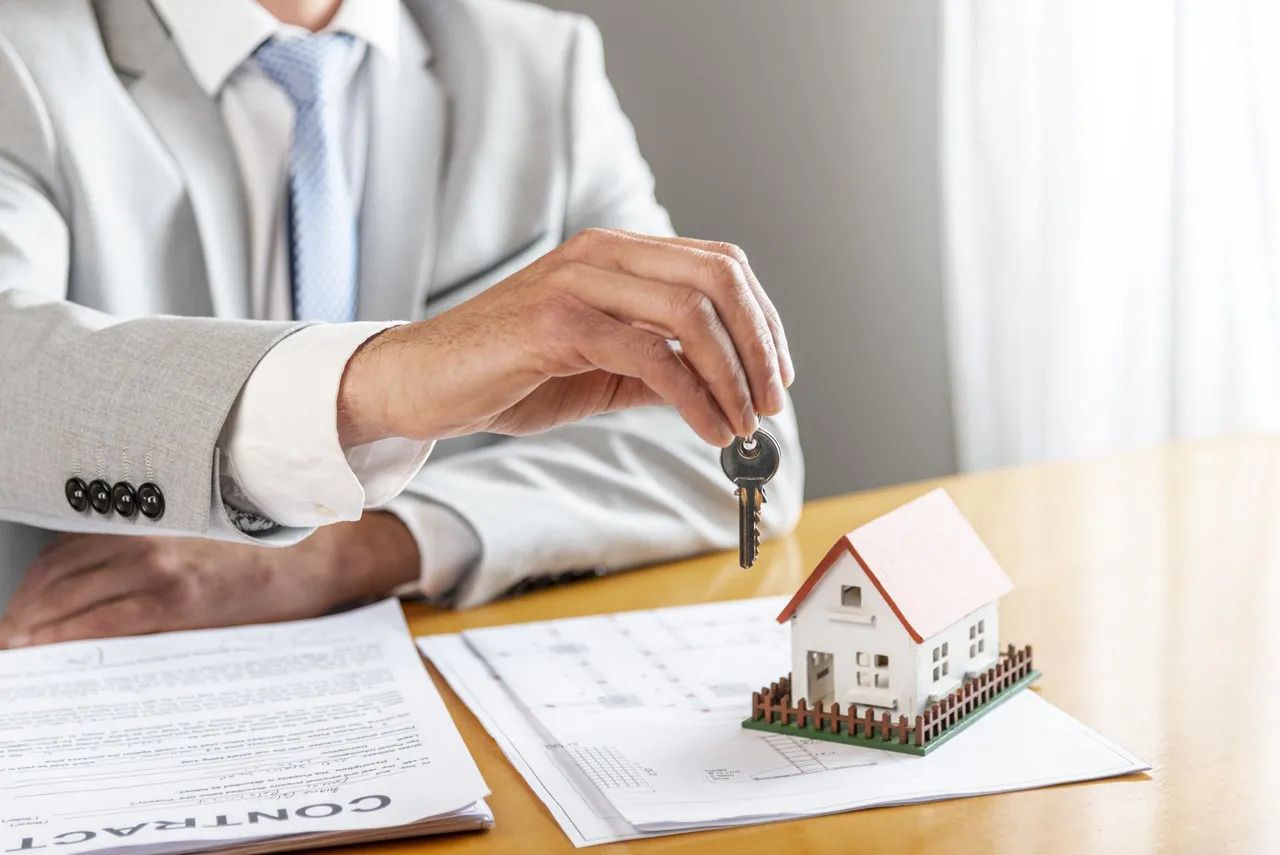 A man is holding a key in front of a model house.