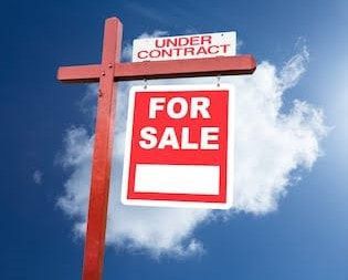 A red and white for sale sign against a blue sky with clouds.