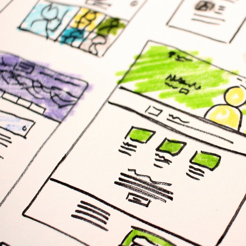 Hand-drawn wireframe sketches of website layouts on paper, featuring colored sections and blocked-out content areas.