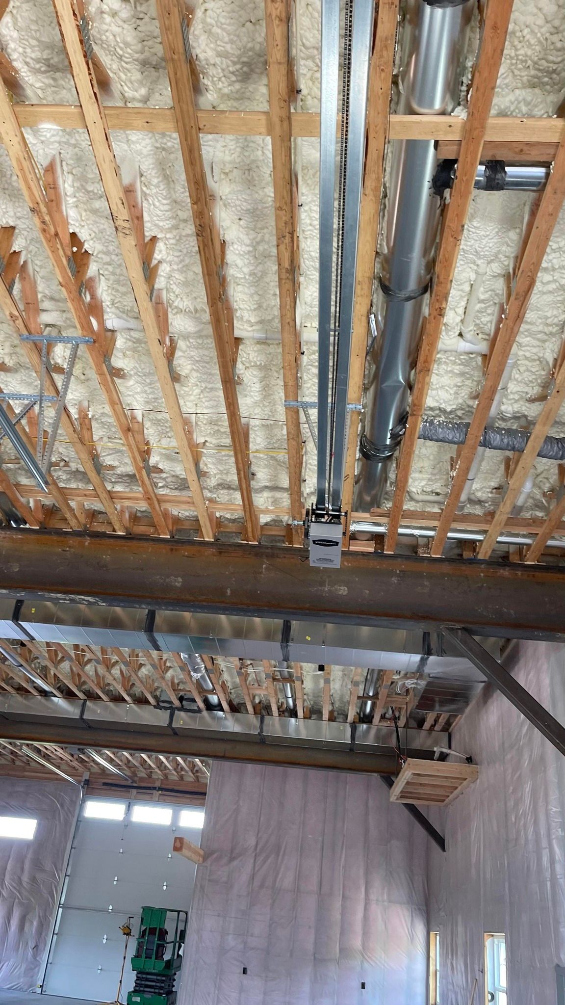A construction view of an interior ceiling with exposed framing, spray foam insulation, metal ducting, and electrical boxes.
