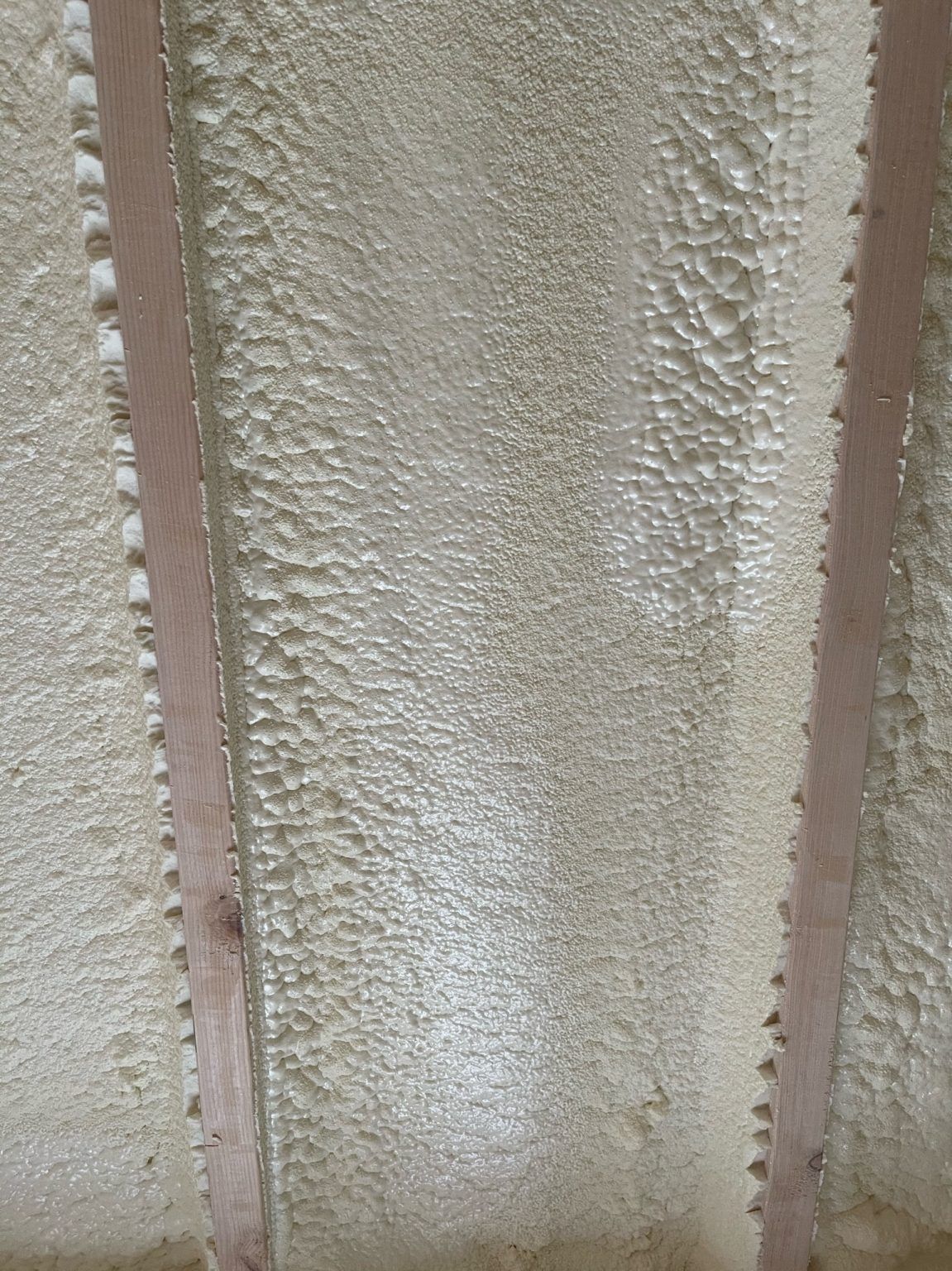 Two vertical wooden studs framing a wall cavity filled with beige spray foam insulation.