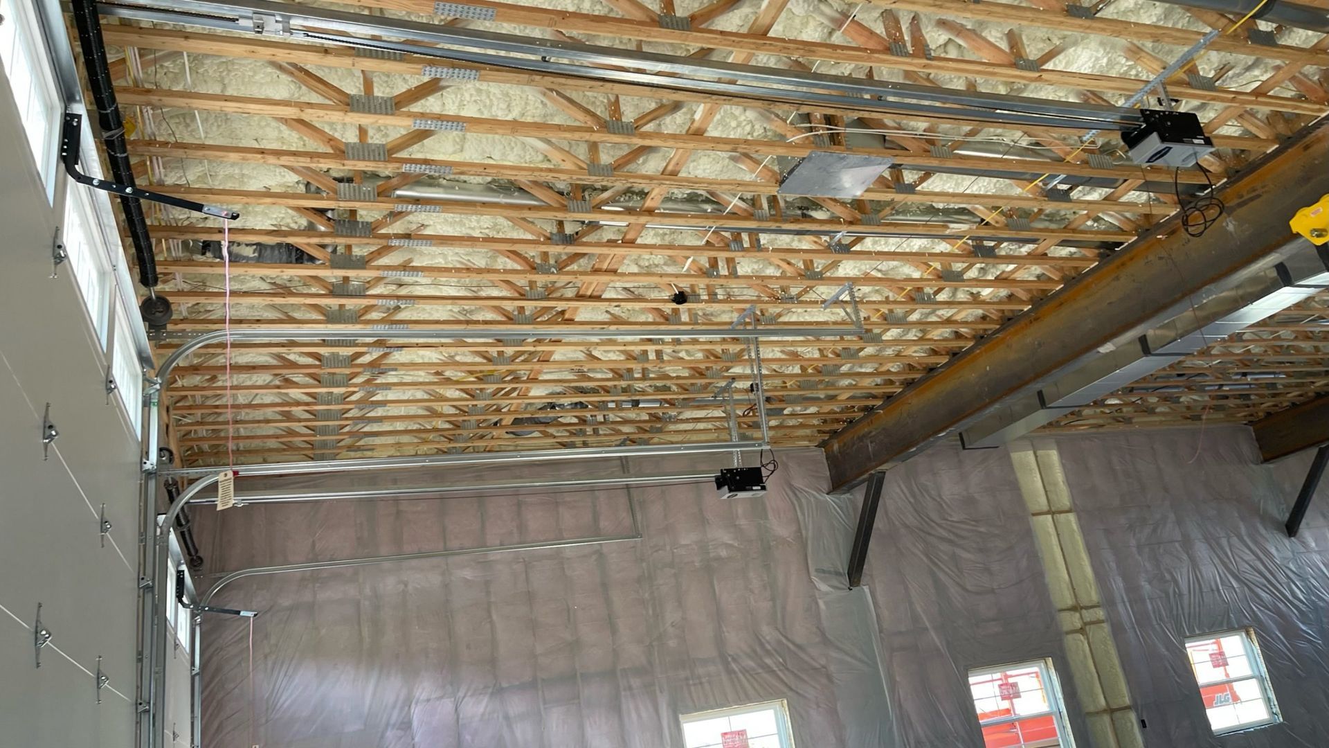A perspective shot looking up at a garage ceiling featuring exposed wooden trusses and insulation.