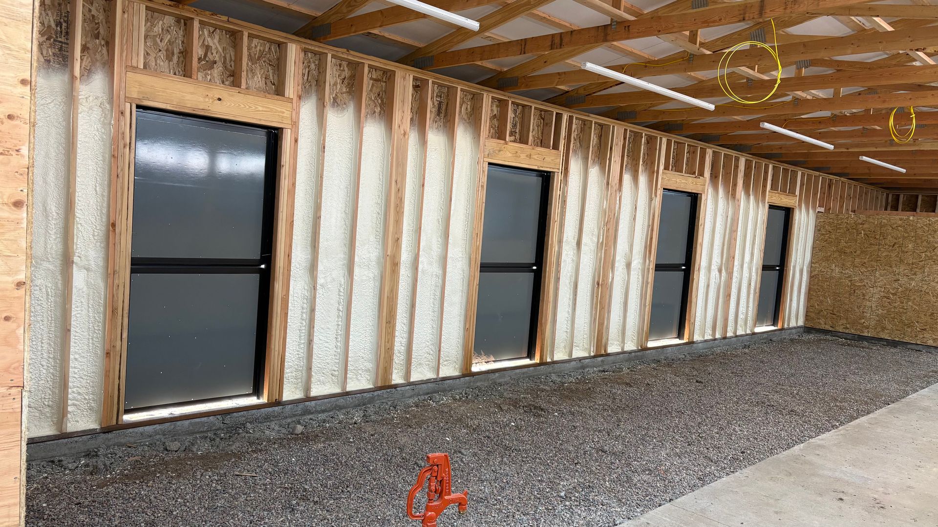 An interior view of a building under construction, featuring spray foam insulation between wall studs and four glass doors.