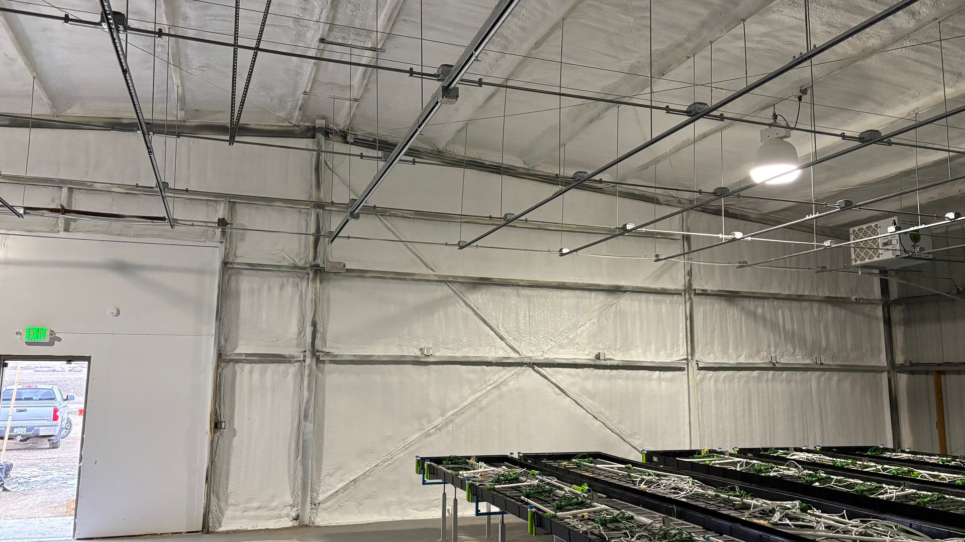 Interior of a large warehouse with insulated white walls, a high ceiling with overhead lights, and rows of plant trays.