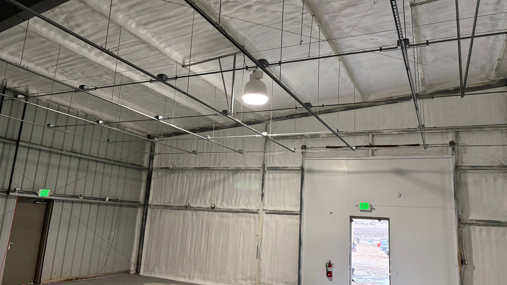 Inside a wide, empty industrial warehouse with white insulated walls, a ceiling light, and two exit doors.