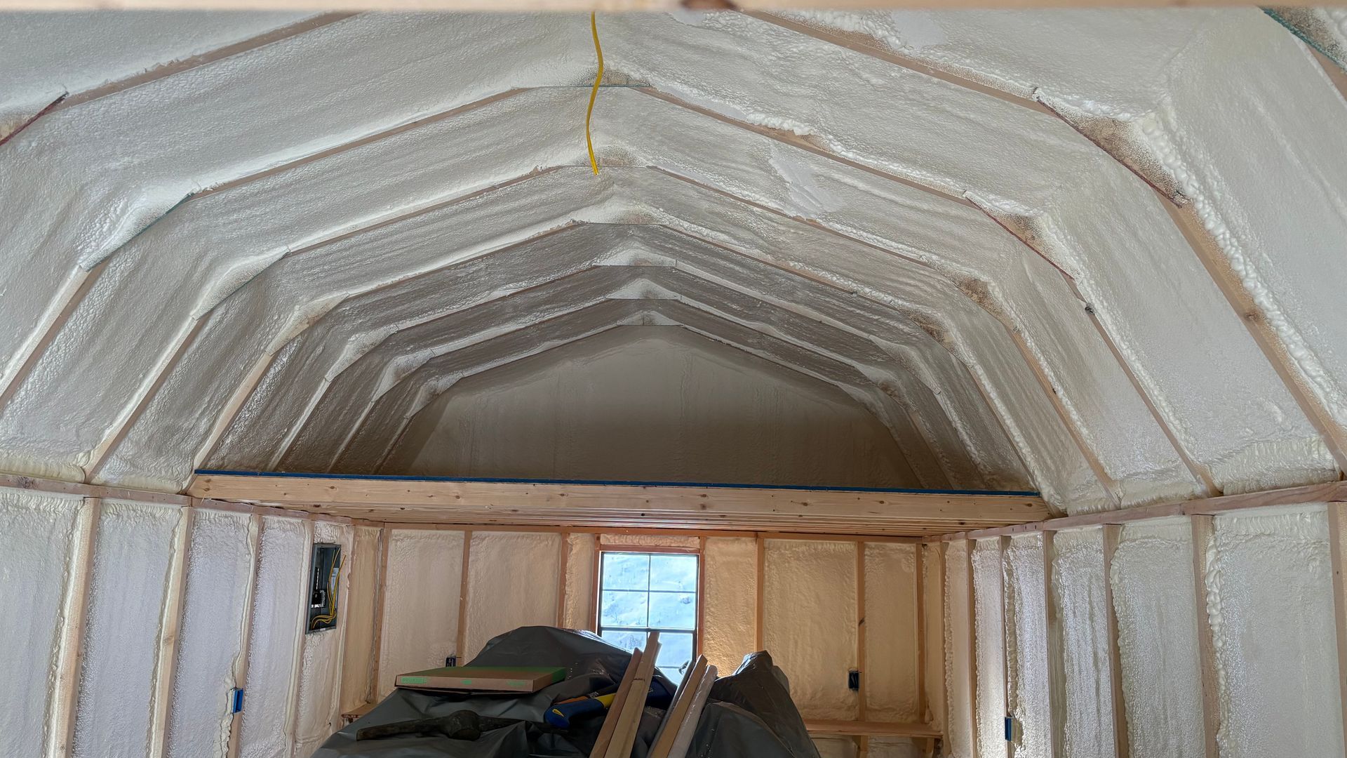 The interior of a shed with gambrel roof framing and walls insulated with spray foam, viewed from a lofted perspective.
