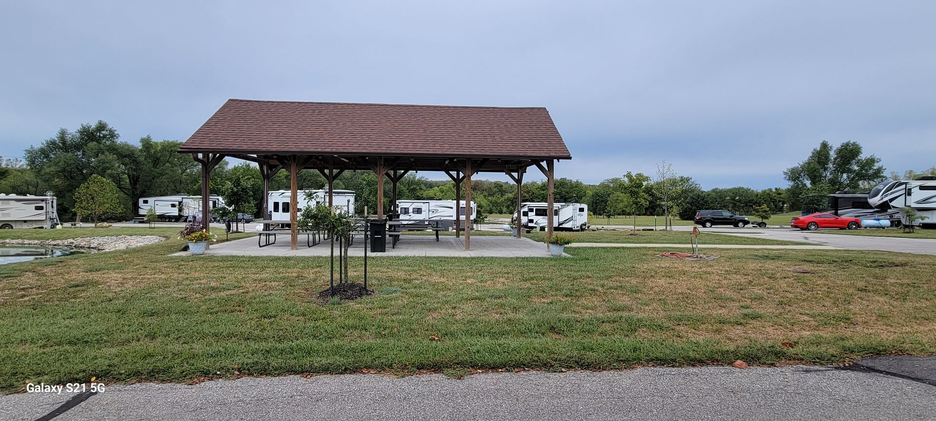A picnic shelter is sitting in the middle of a grassy field.