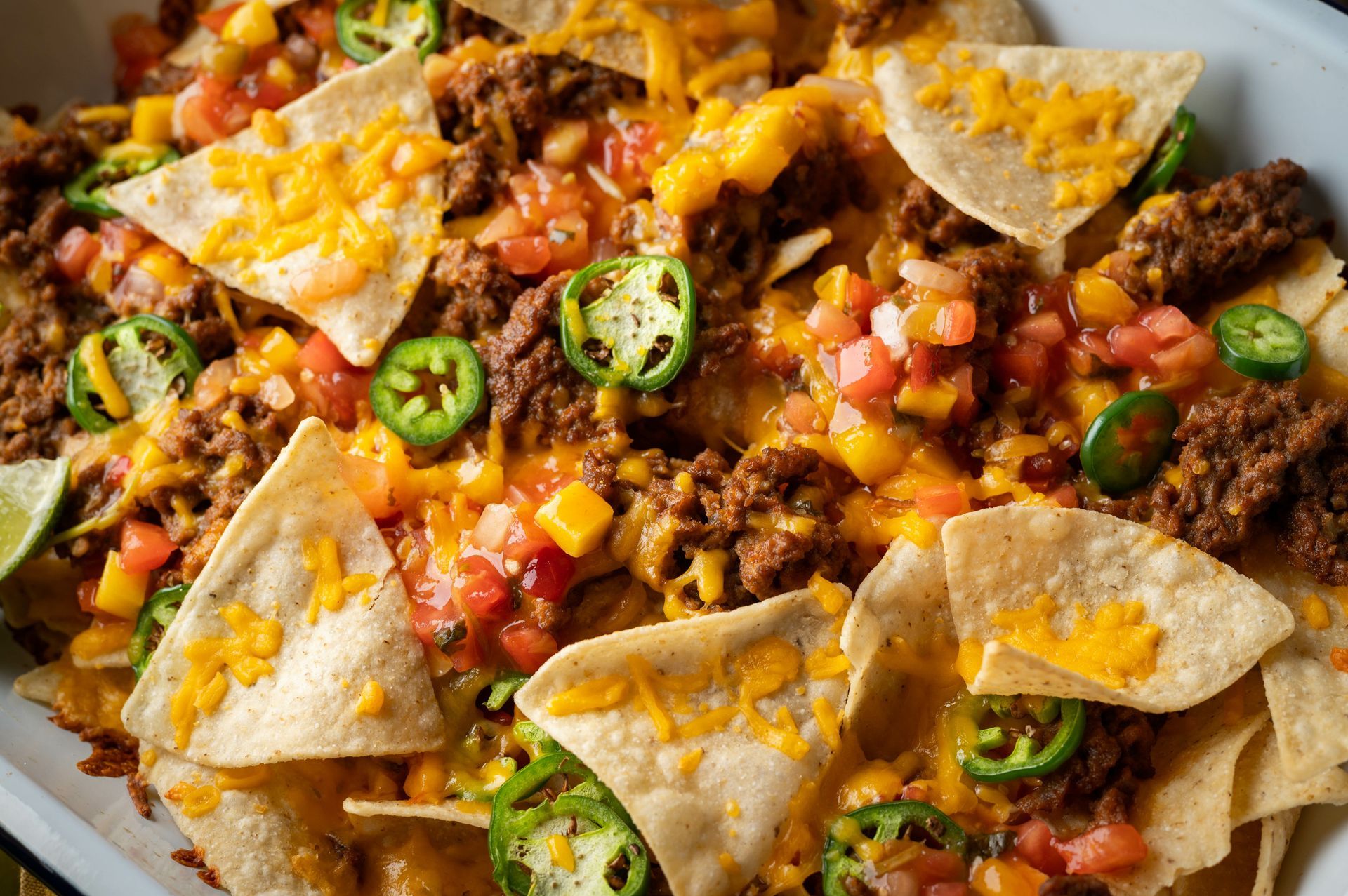 A close up of a plate of nachos with meat , cheese , tomatoes and jalapenos.